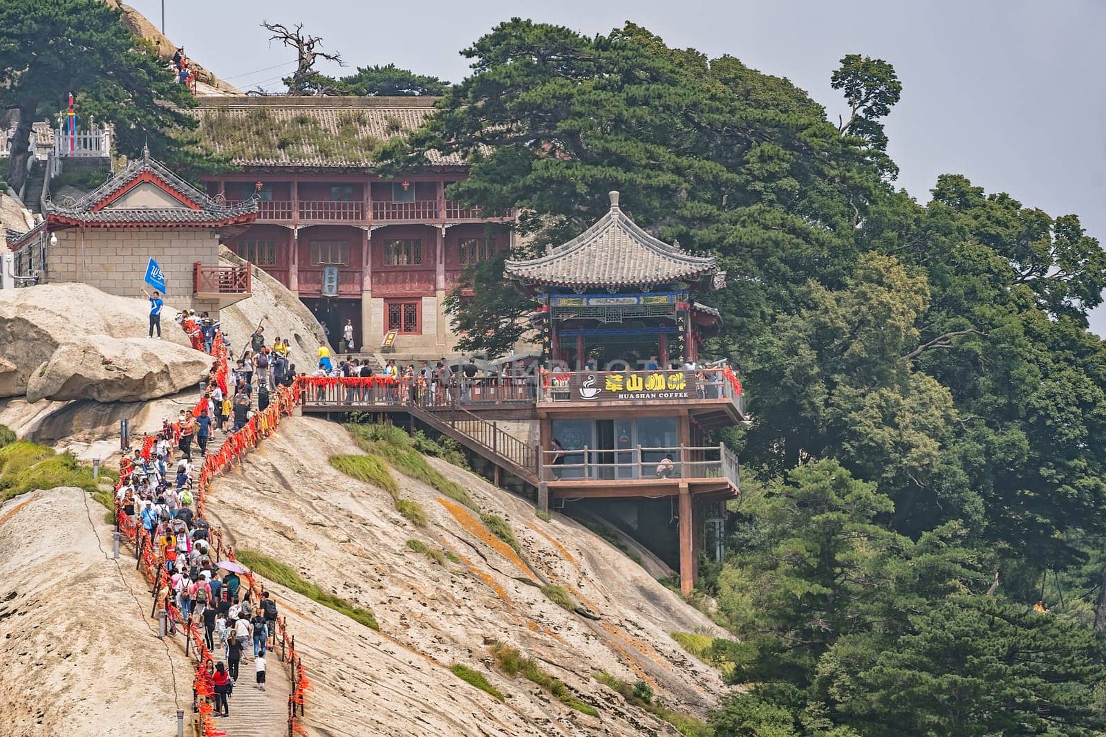 Huashan, China -  August 2019 : Crowds of tourists walking on a narrow ridge on a mountain trail to the West Peak on Huashan mountain, Xian, Shaanxi Province