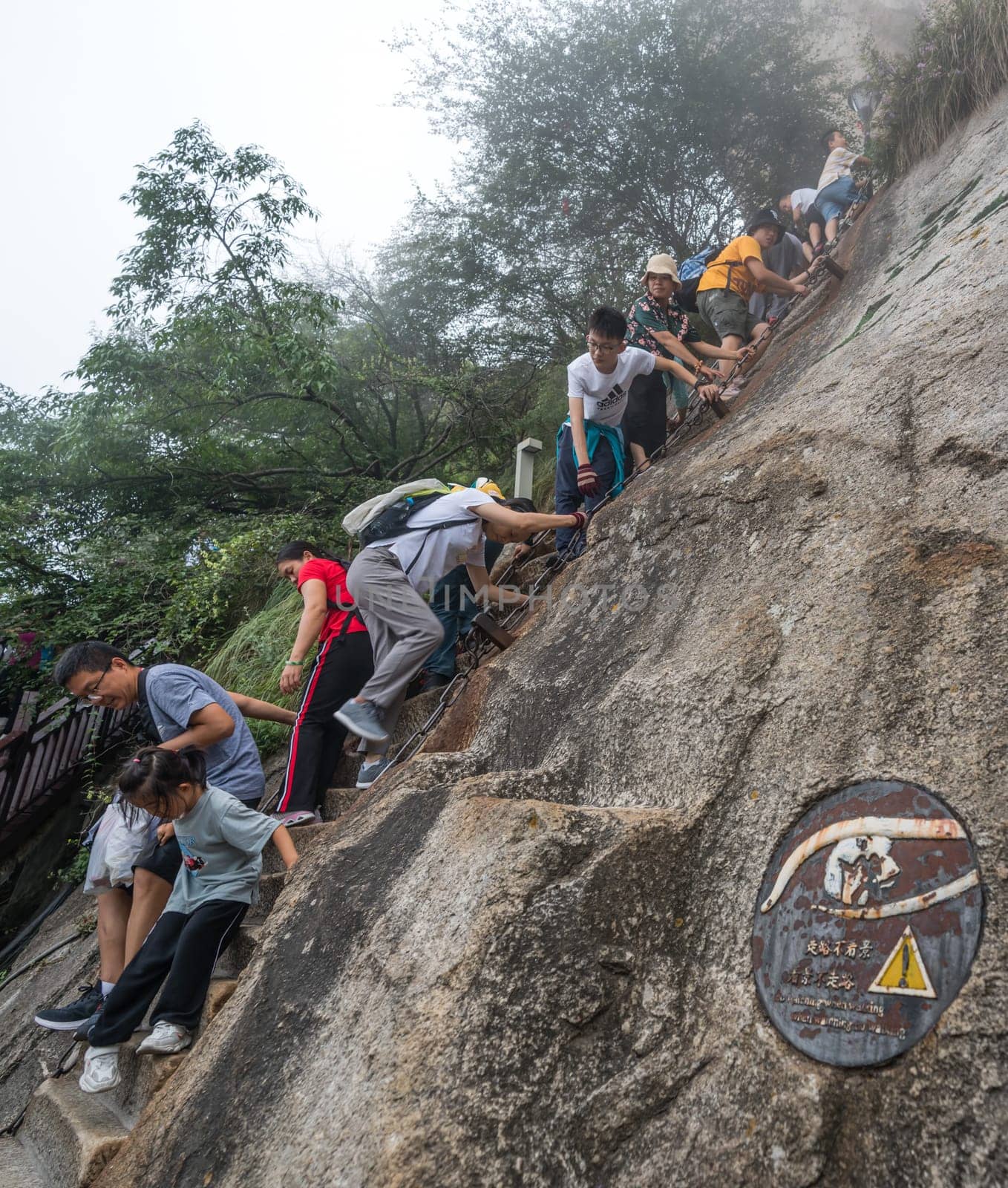 Huashan, China -  August 2019 : Tourists climbing up the vertical, steep, cut into rocky edge stairs on a mountain trail to the North and West Peak on Huashan mountain, Xian, Shaanxi Province