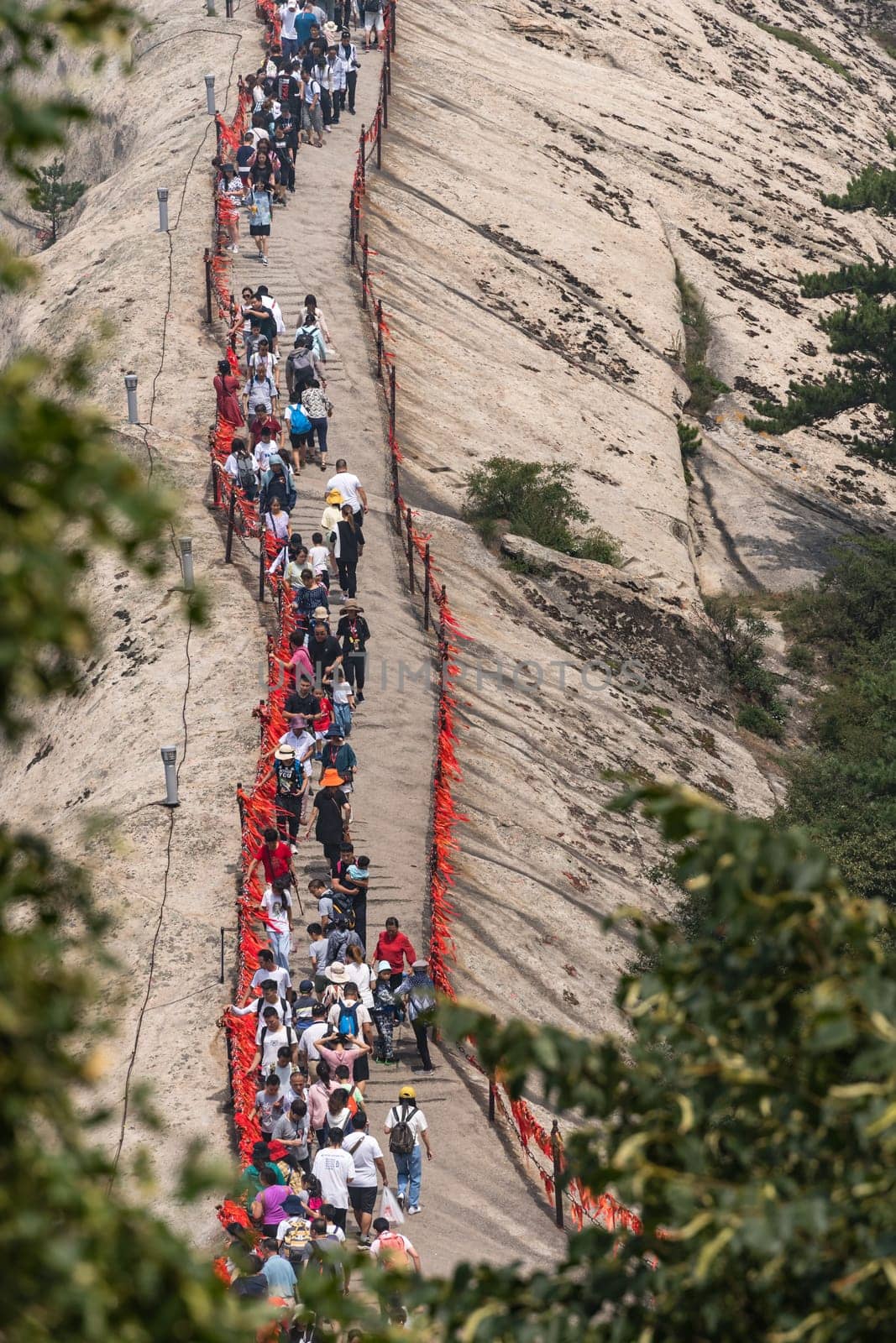 Huashan, China -  August 2019 : Crowds of tourists walking on a narrow ridge on a mountain trail to the West Peak on Huashan mountain, Xian, Shaanxi Province