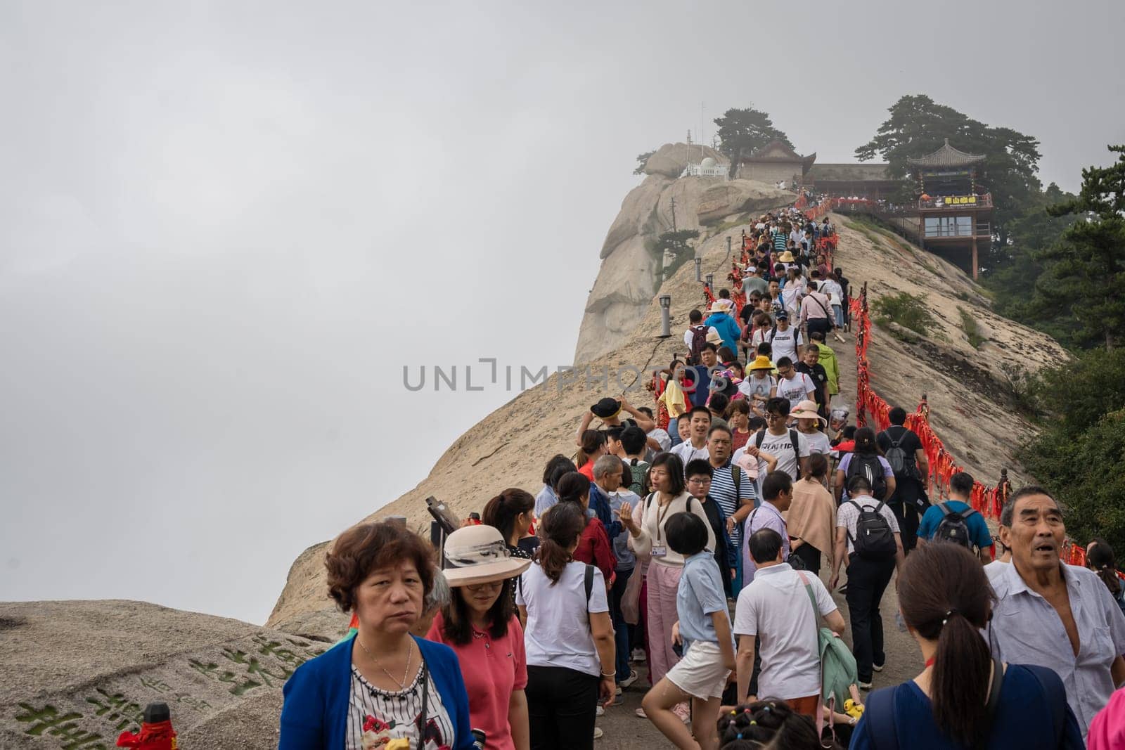 Huashan, China -  August 2019 : Crowds of tourists walking on a narrow ridge on a mountain trail to the West Peak on Huashan mountain, Xian, Shaanxi Province