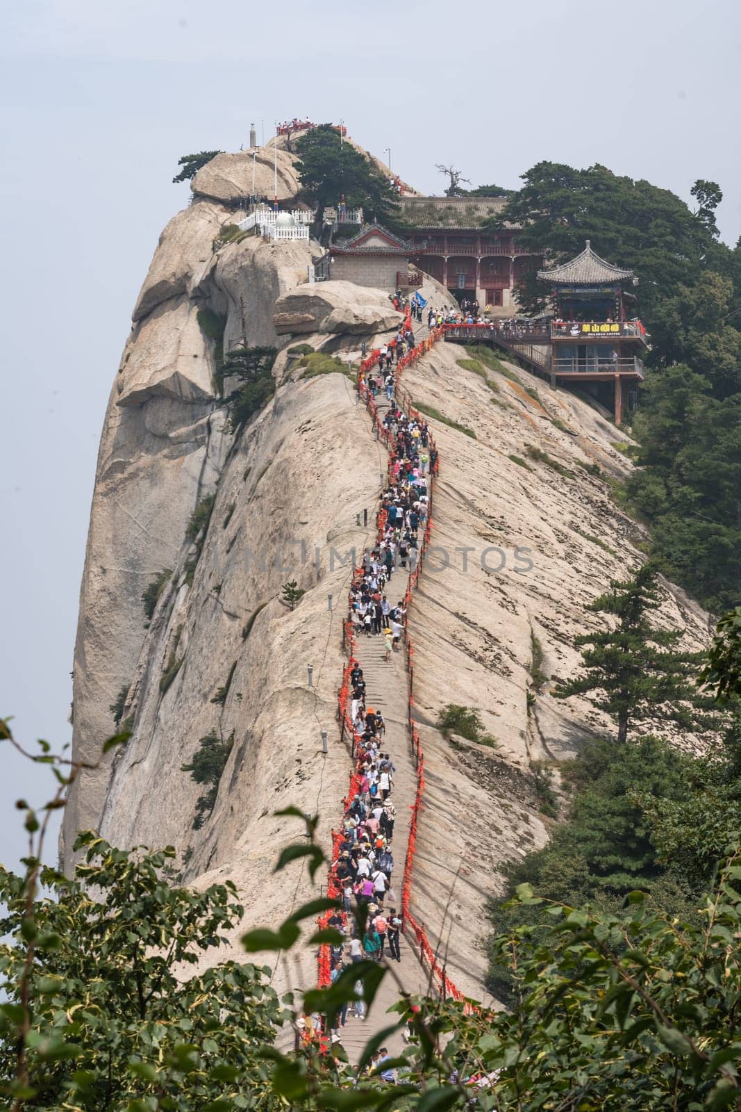 Huashan, China -  August 2019 : Crowds of tourists walking on a narrow ridge on a mountain trail to the West Peak on Huashan mountain, Xian, Shaanxi Province
