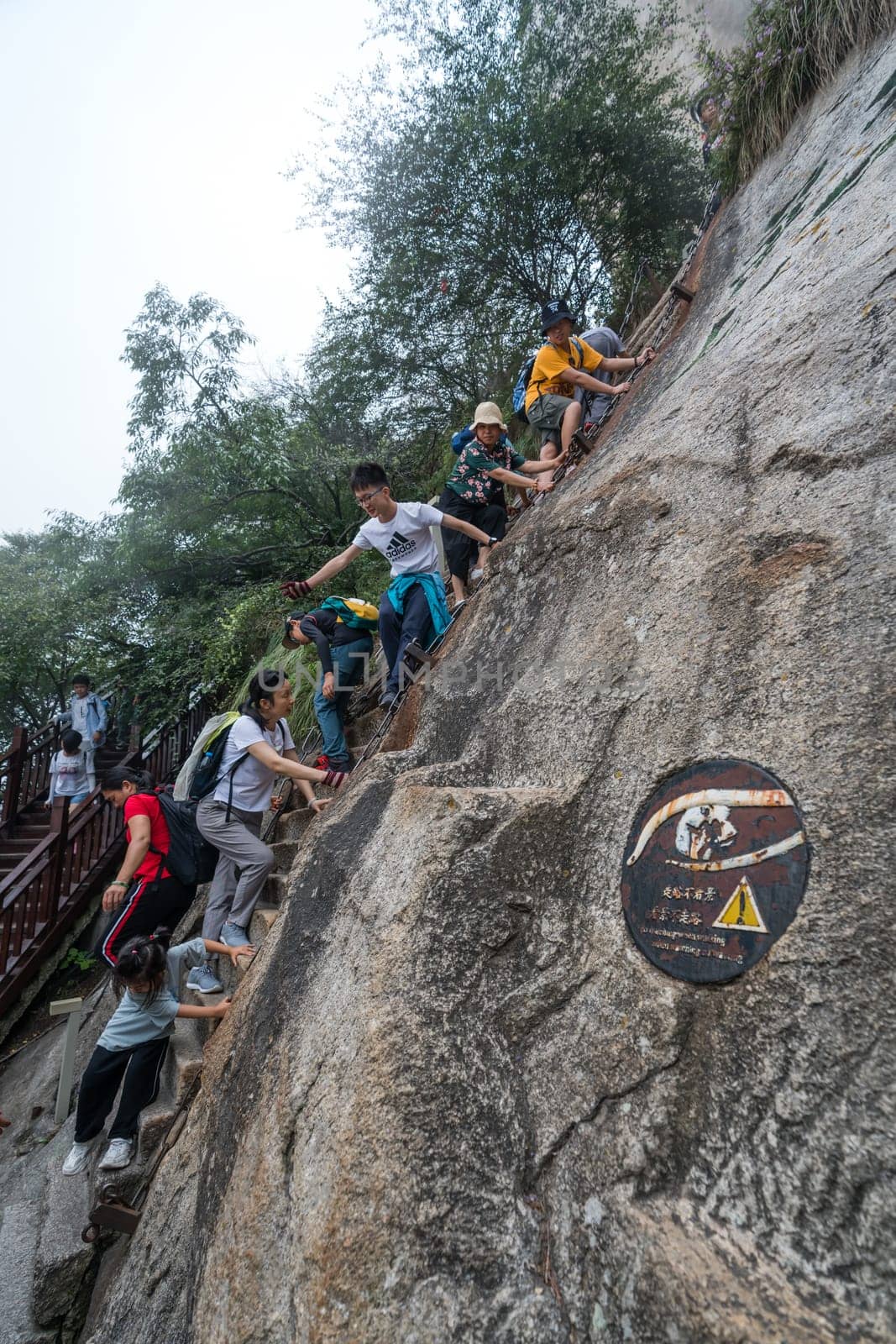 Huashan, China -  August 2019 : Tourists climbing up the vertical, steep, cut into rocky edge stairs on a mountain trail to the North and West Peak on Huashan mountain, Xian, Shaanxi Province