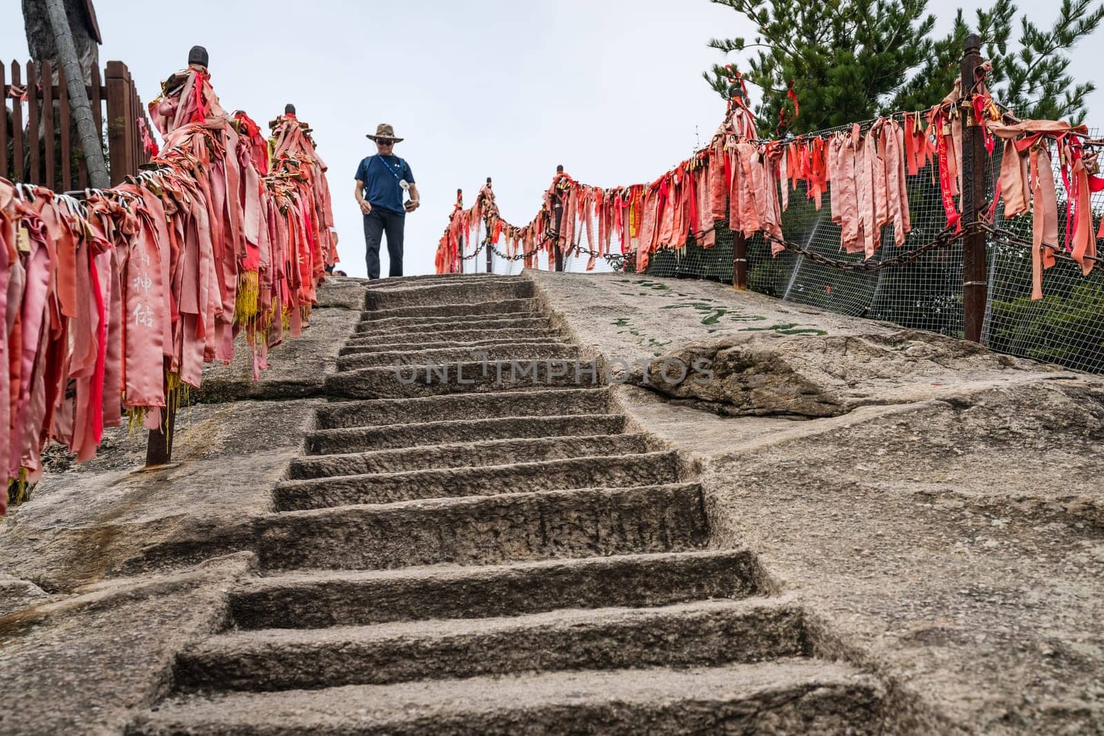 Huashan, China -  August 2019 : Male tourist with a hat walking down on the cut in a rock stone stairs steps leading to the summit of a West Peak on Huashan mountain, Xian, Shaanxi Province