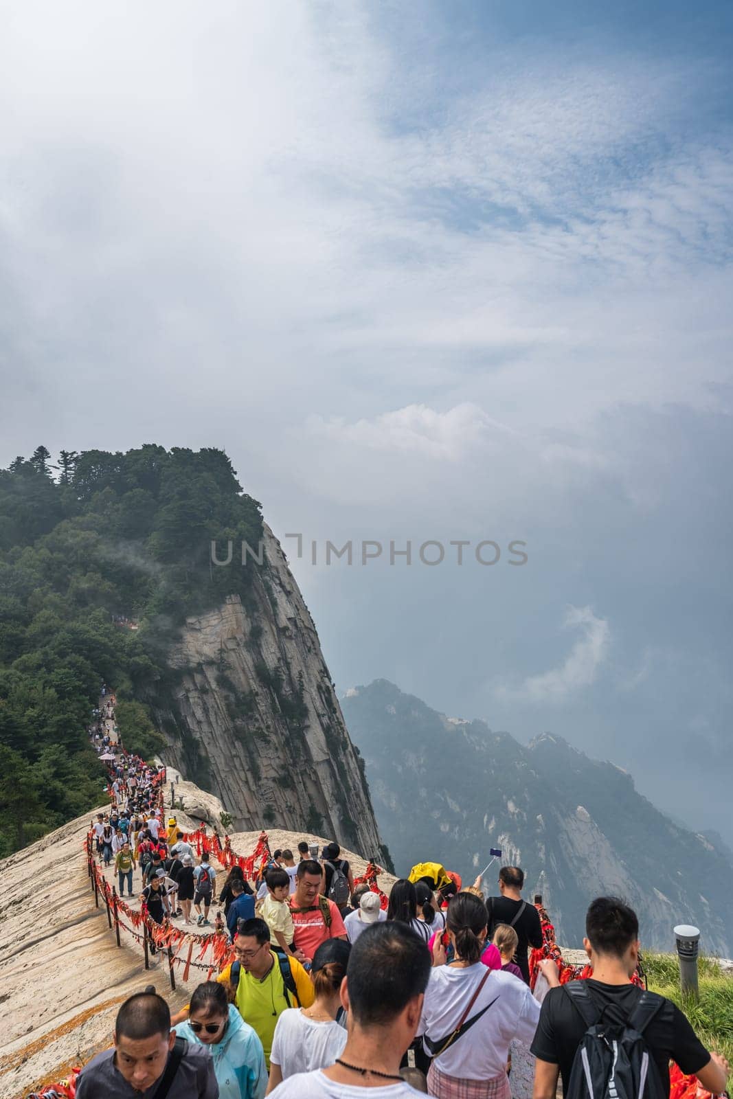 Huashan, China -  August 2019 : Crowds of tourists walking on a narrow ridge on a mountain trail to the West Peak on Huashan mountain, Xian, Shaanxi Province