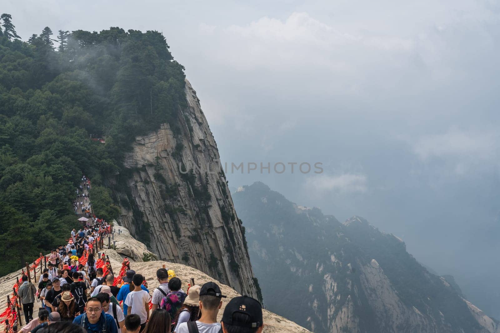 Huashan, China -  August 2019 : Crowds of tourists walking on a narrow ridge on a mountain trail to the West Peak on Huashan mountain, Xian, Shaanxi Province