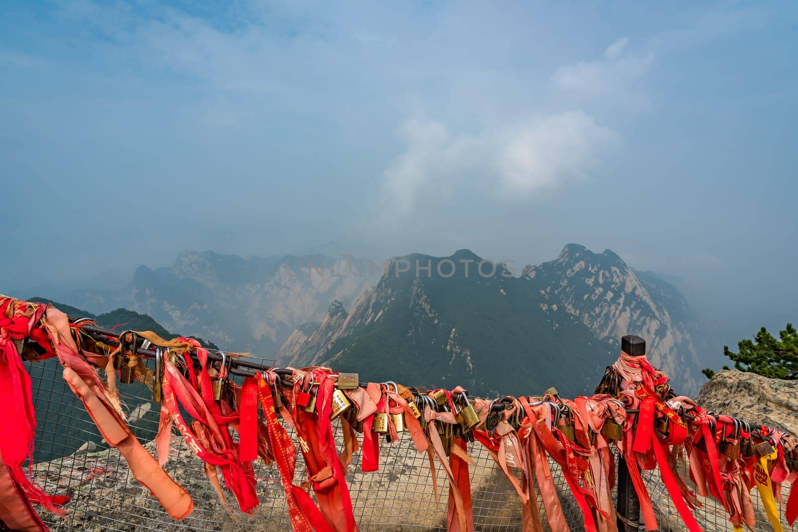Huashan, China -  August 2019 : Red and yellow ribbons attached to the protective barrier on a lookout with the stunning mountain landscape view from the summit of West Peak, Huashan mountain, Shaanxi Province