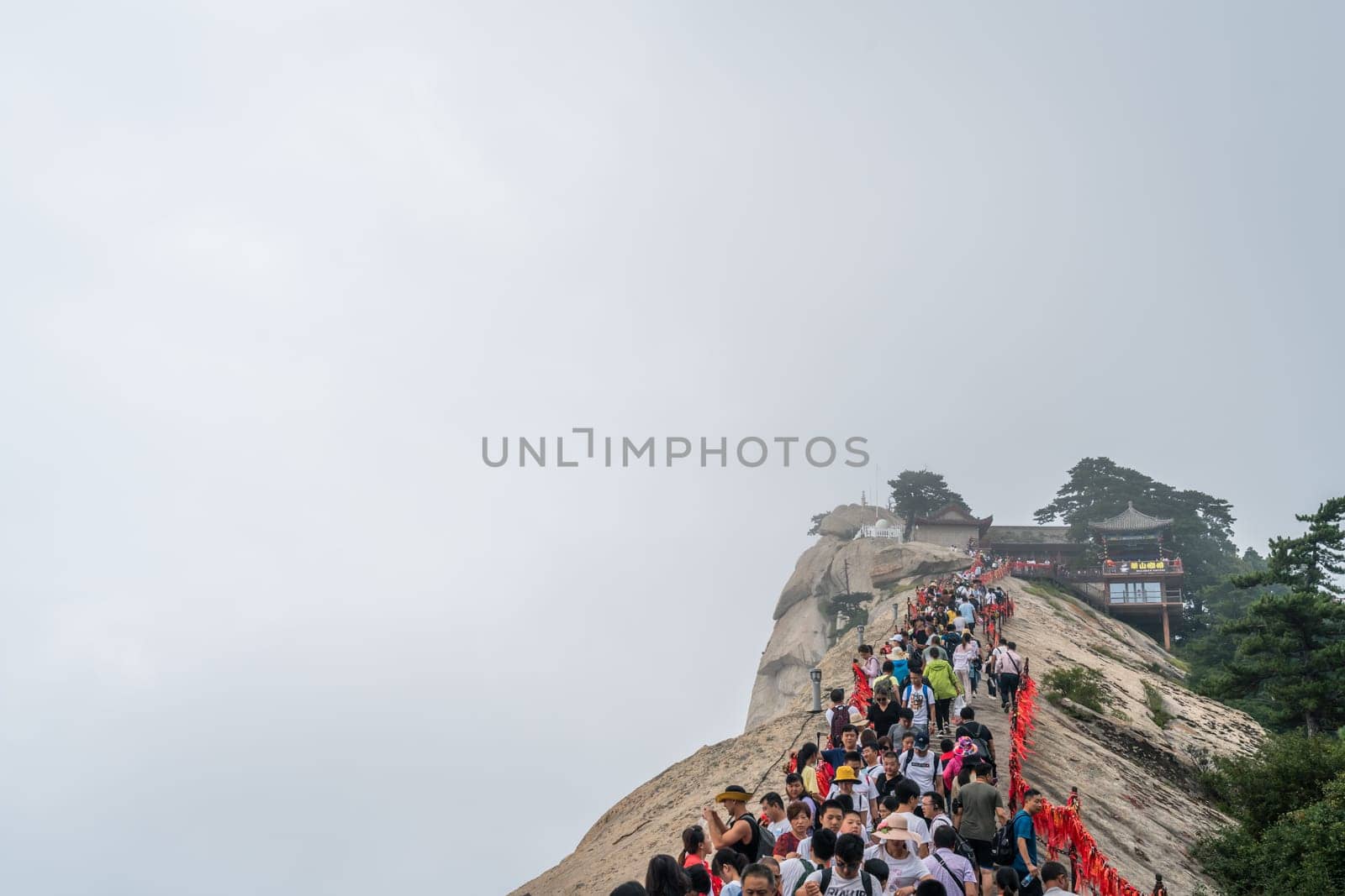 Huashan, China -  August 2019 : Crowds of tourists walking on a narrow ridge on a mountain trail to the West Peak on Huashan mountain, Xian, Shaanxi Province