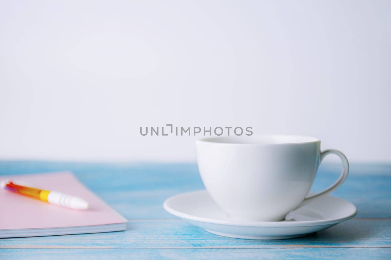 A cup of coffee with notebook on wooden blurred background