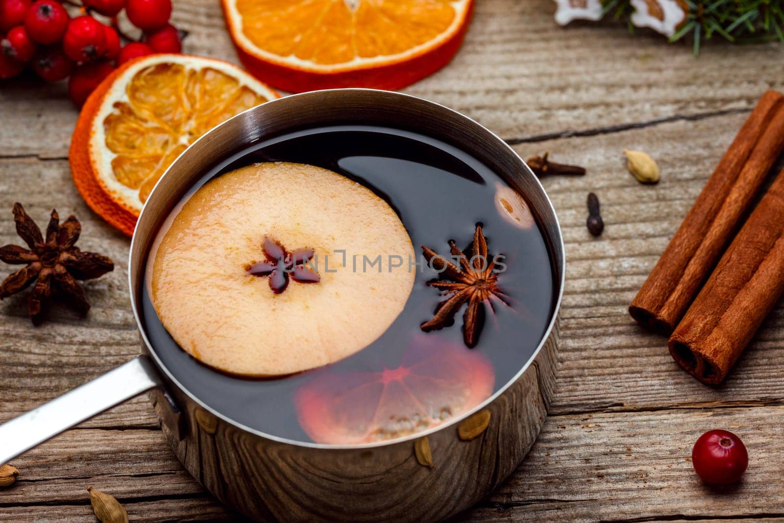Small stewpot with mulled wine and cinnamon sticks, slice of oranges and apple on wooden table top view. Hot winter drink. Christmas beverage.