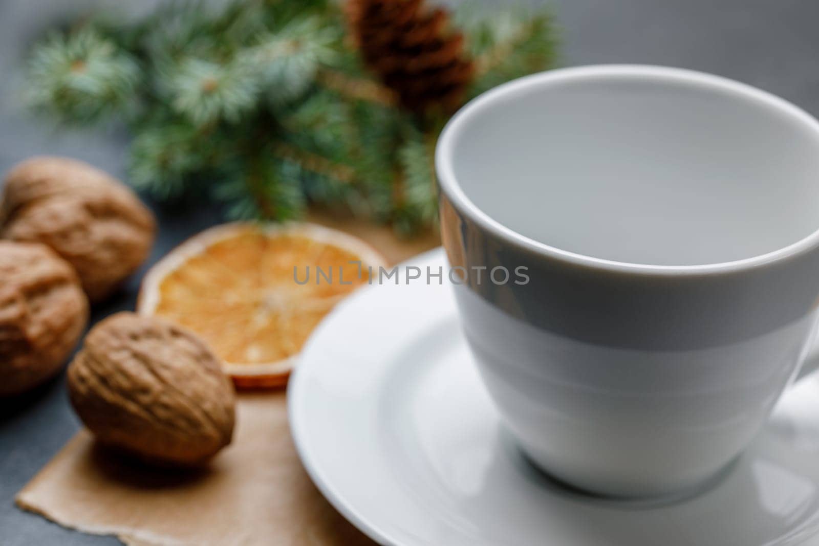White cup and saucer on a Christmas background with walnuts, a slice of orange, with shallow depth of field