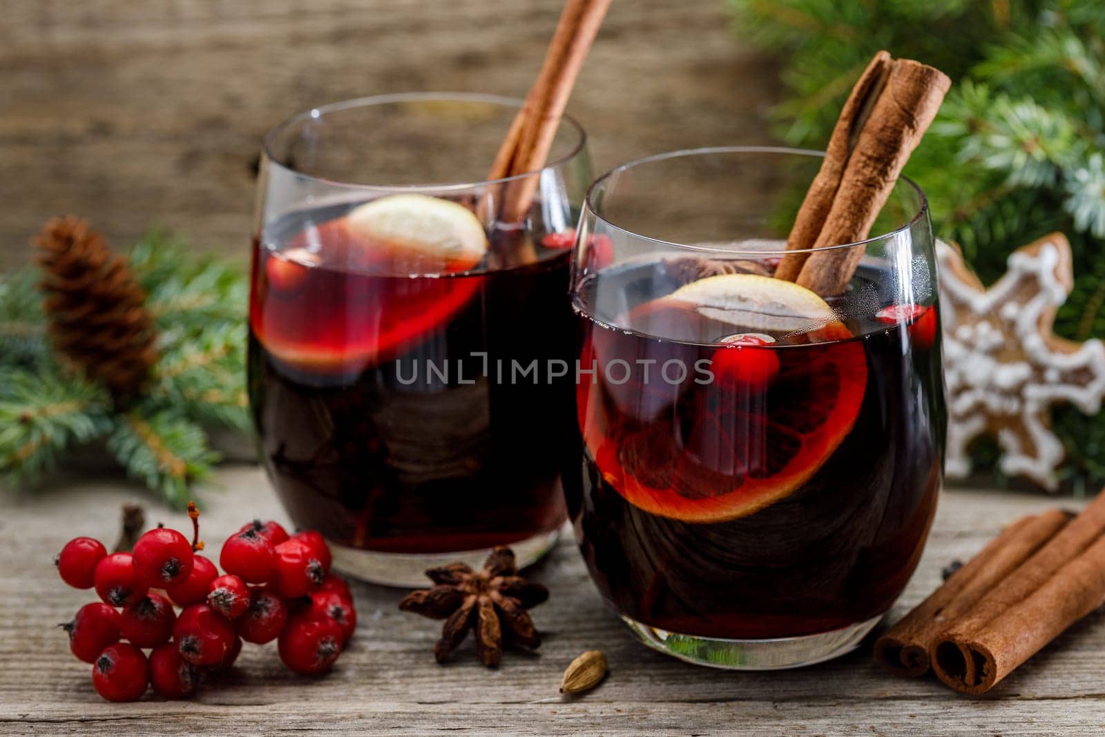 Mulled wine in glasses in a Christmas setting with dry slices of oranges, cookies in the shape of a snowflake, red berries and cinnamon