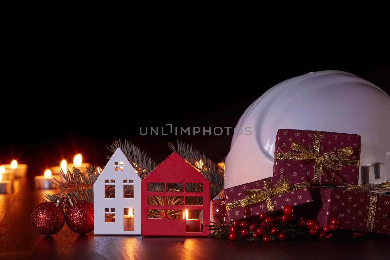 White construction hard hat, candles, gift boxes, fir branch and Christmas ornament on black background. Construction New Year, Christmas background with copy space. For greeting card or advertising