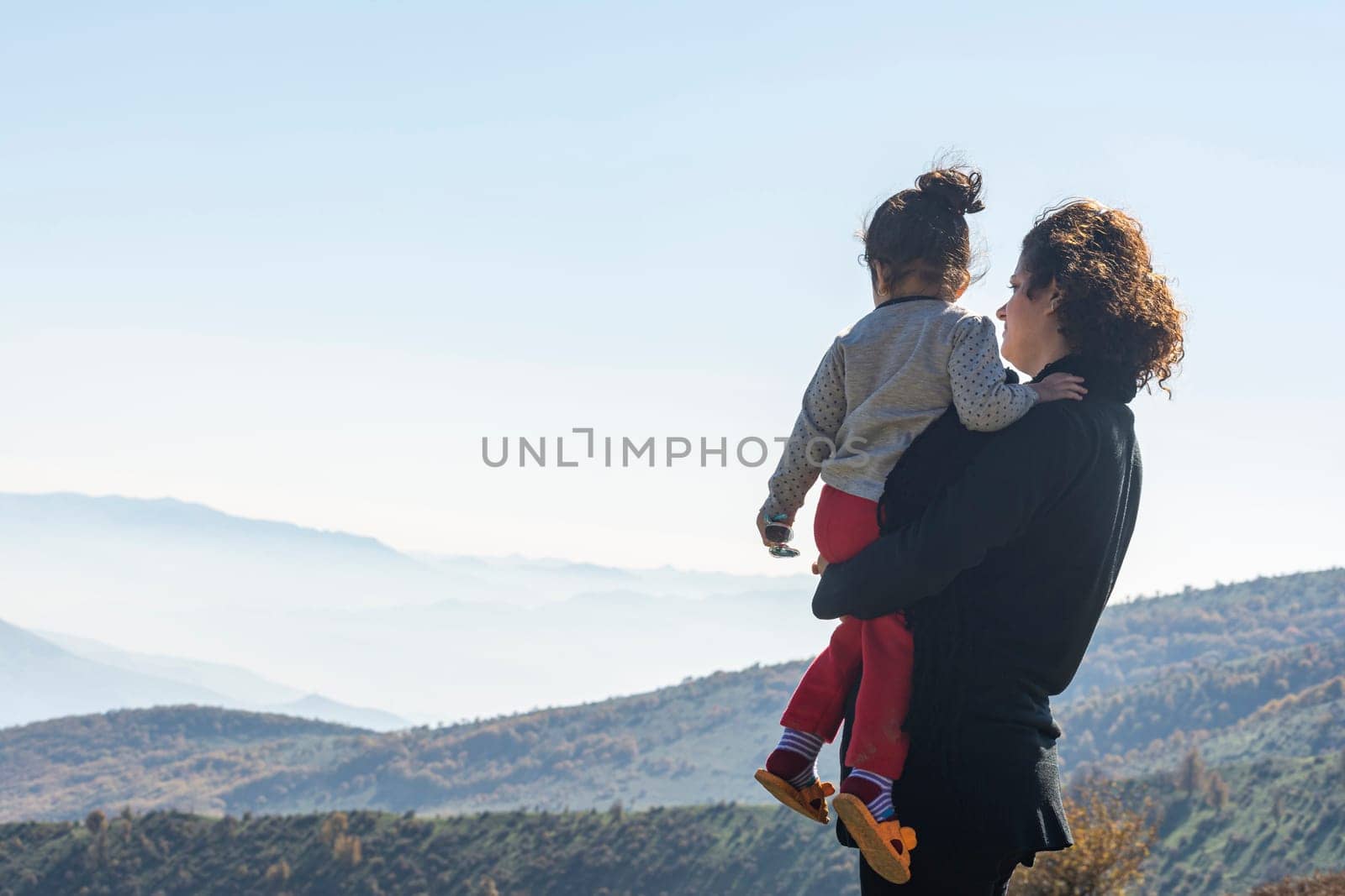 Young mother with little daughter looking at mountains on vacation, family travel together on top of high mountain outdoors, looking at beautiful landscape. Rear viewpoint