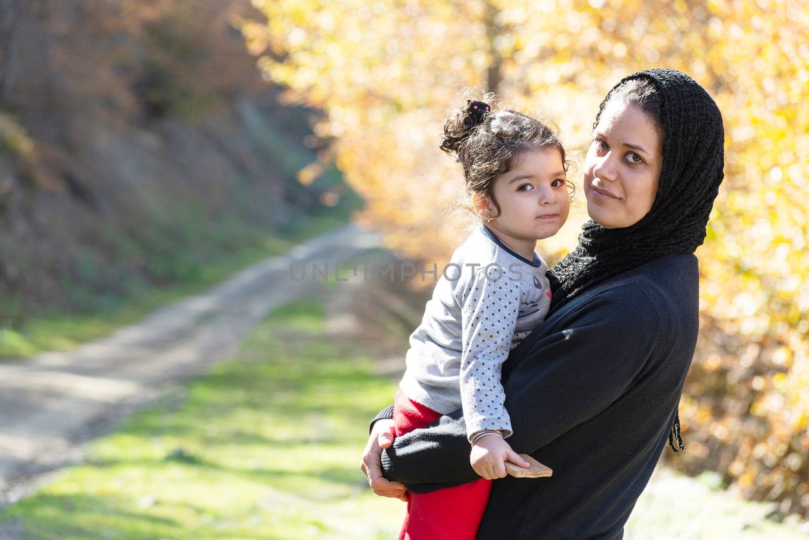 Young mother and a little girl in her hug portrait in autumn nature scene landscape