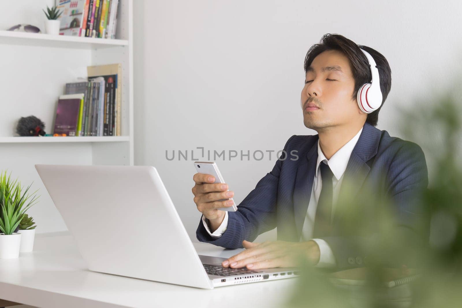 Asian Businessman Listen to Music by Headphone with Tree Foreground. Relax time of Asian businessman in office