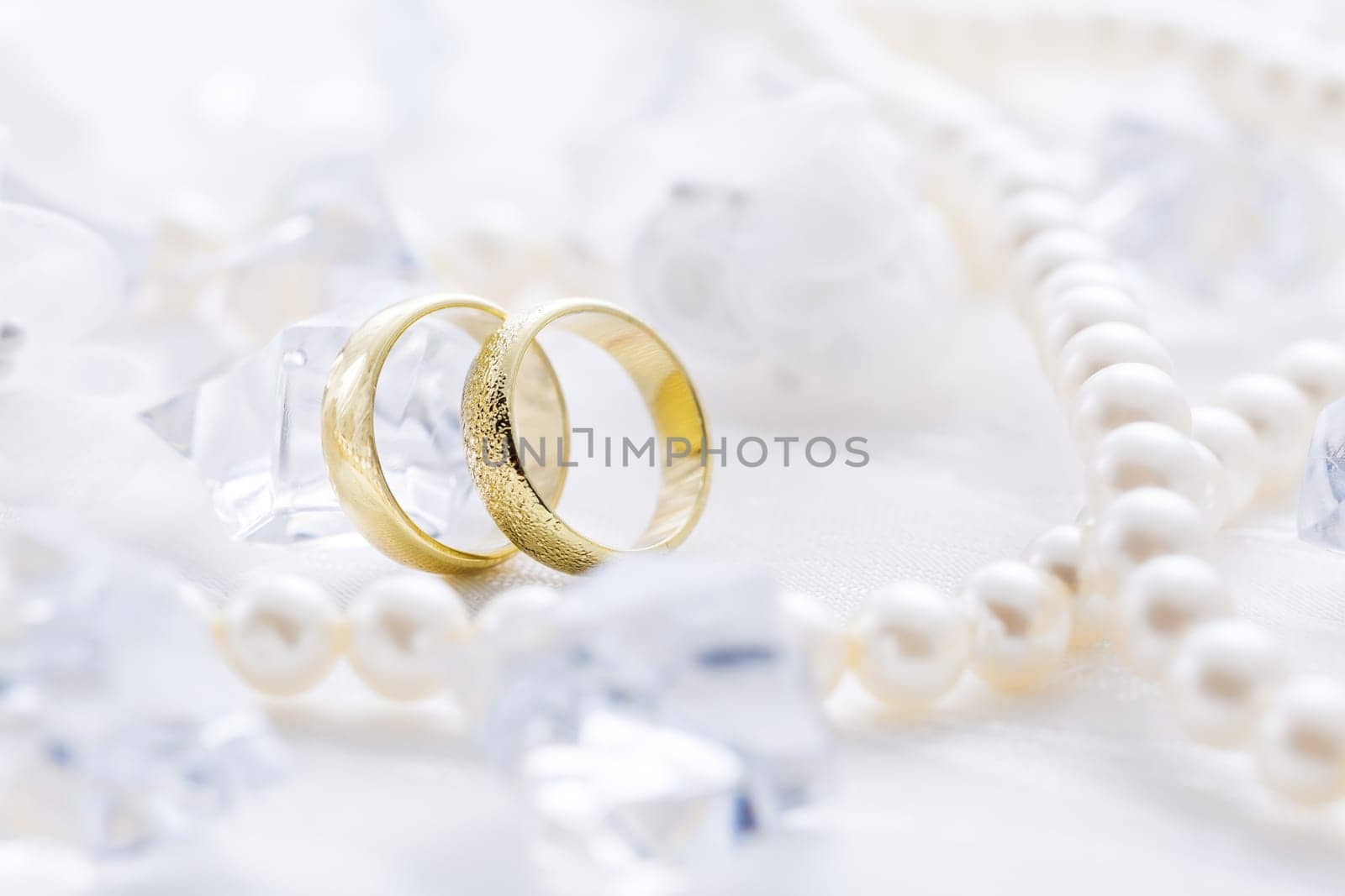Two golden rings with pearl necklace and on white background as symbol of love and marriage