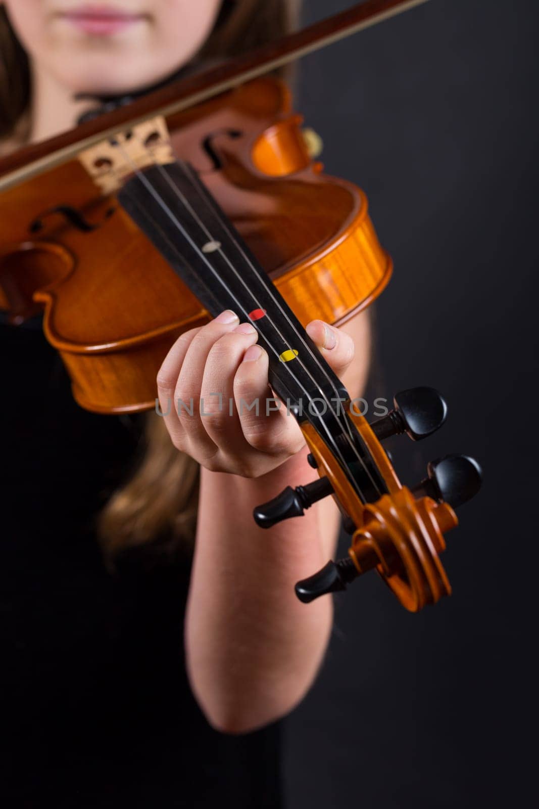 Close up of professional violin in hands of little girl playing it on black background