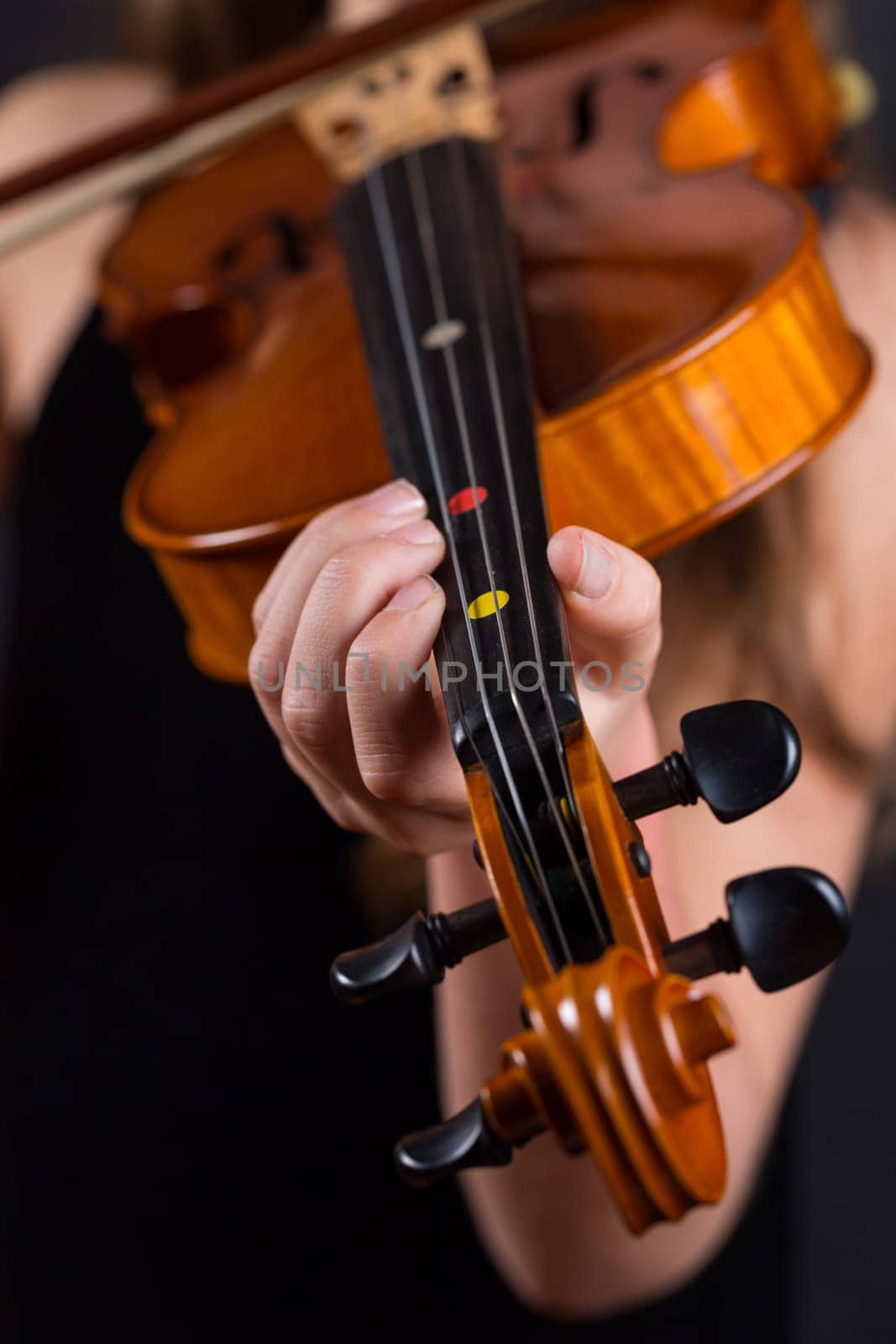 Close up of professional violin in hands of little girl playing it on black background