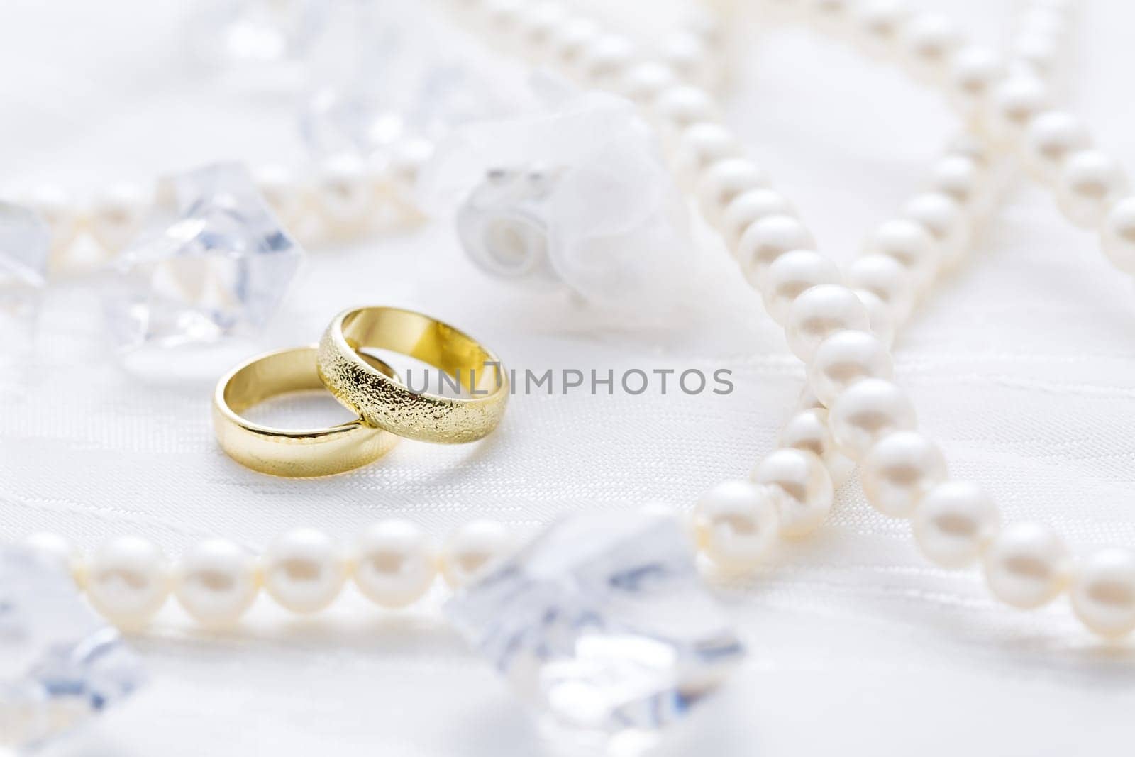 Two golden rings with pearl necklace and on white background as symbol of love and marriage