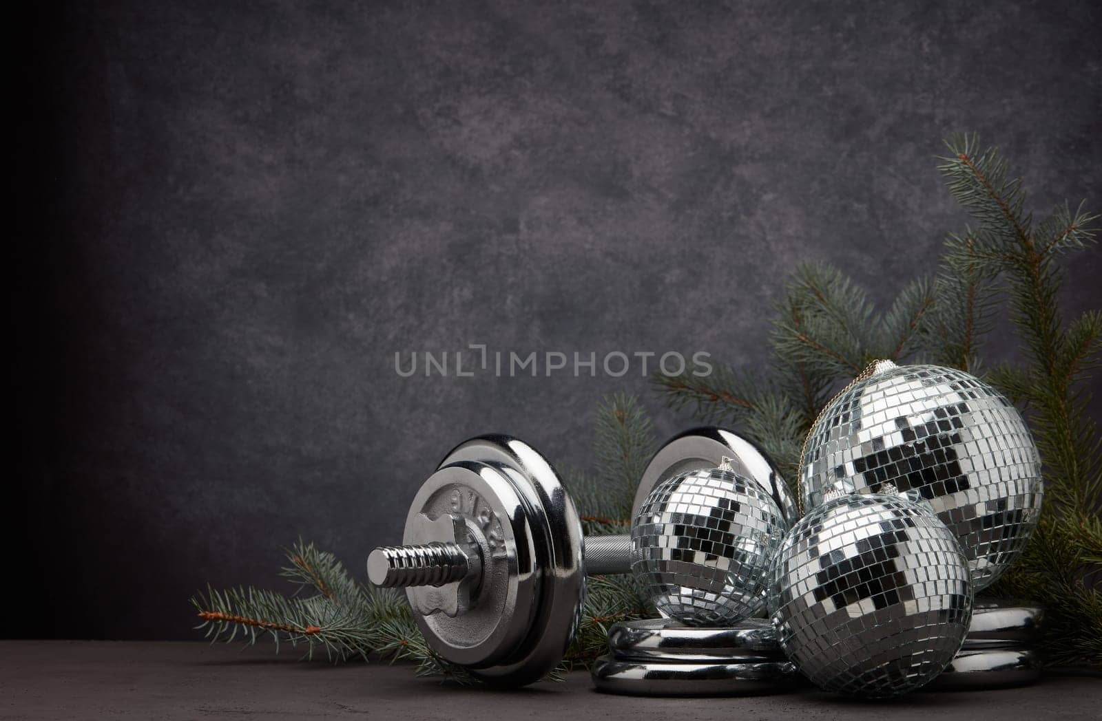 Sports equipment (dumbbell with weights), fir branch, Christmas ornament on dark grey background with copy space. Fitness, sport or healthy lifestyle concept. New Year and Christmas.