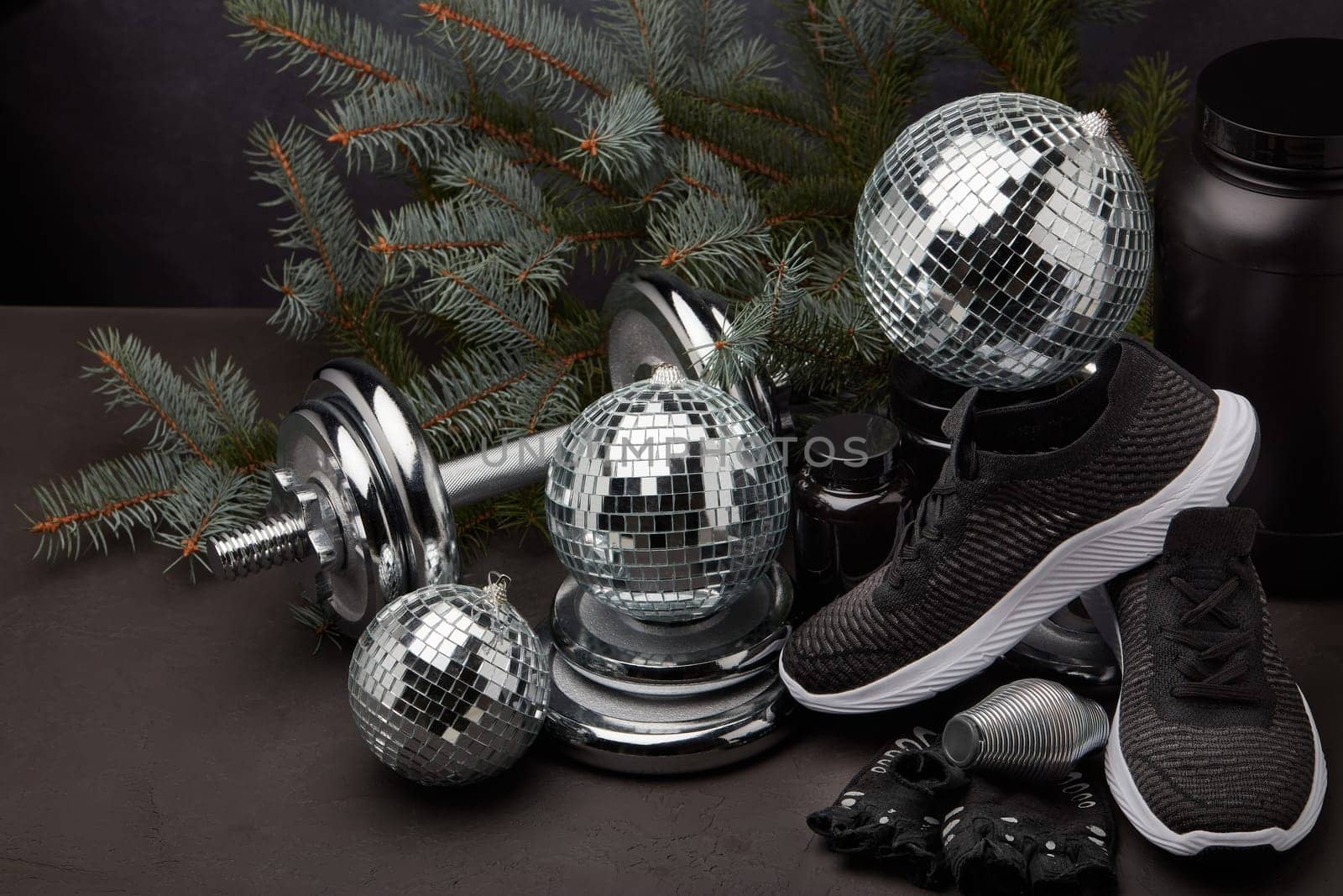 Sports nutrition (supplements), sports equipment, branch of fir, Christmas ornaments on dark grey background. Fitness, sport or healthy lifestyle concept. New Year and Christmas.