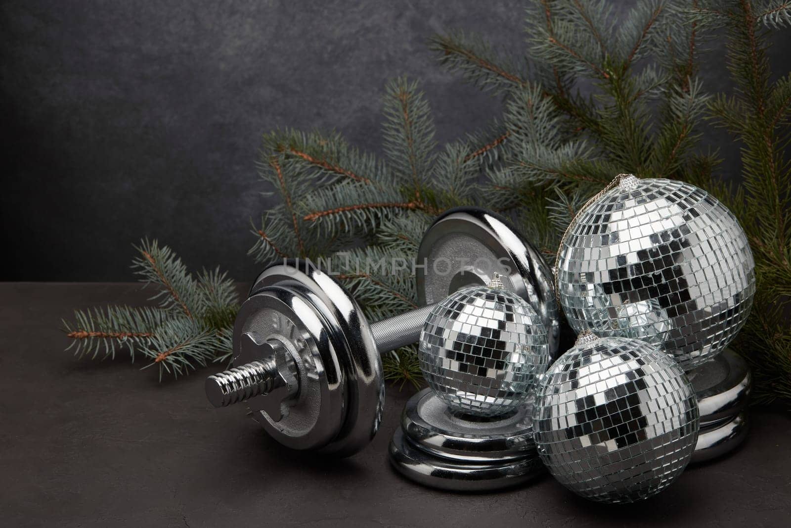 Sports equipment (dumbbell with weights), fir branch, Christmas ornament on dark grey background. Fitness, sport or healthy lifestyle concept. New Year and Christmas.