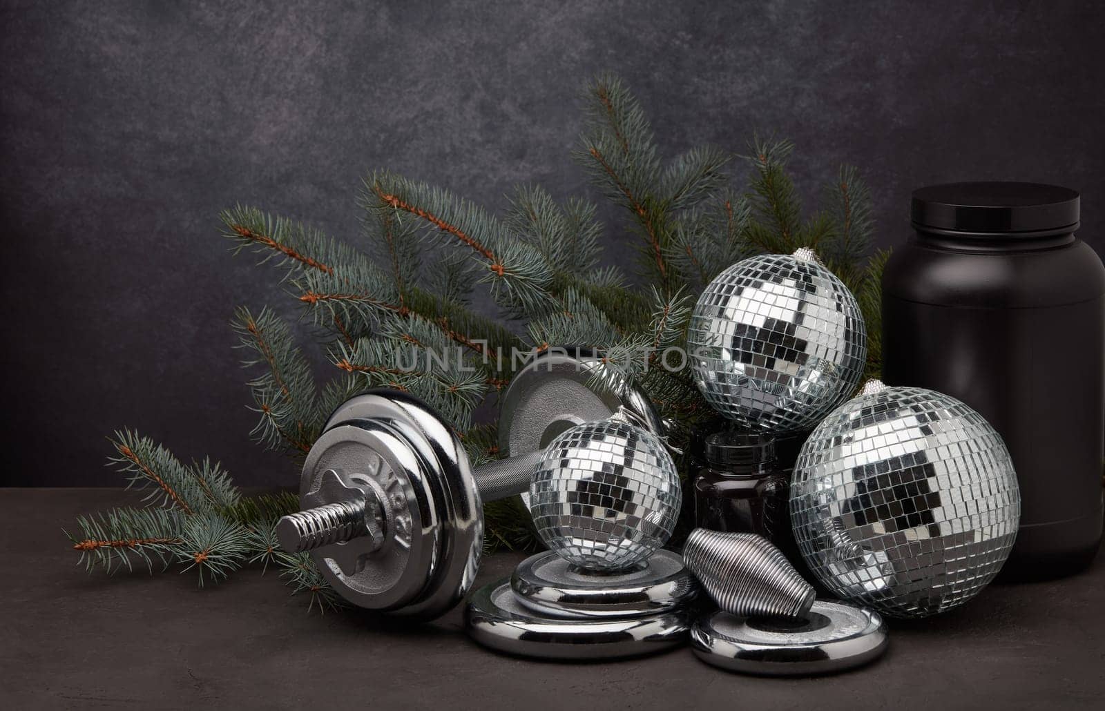 Sports nutrition (supplements), sports equipment, branch of fir, Christmas ornaments on dark grey background. Fitness, sport or healthy lifestyle concept. New Year and Christmas.