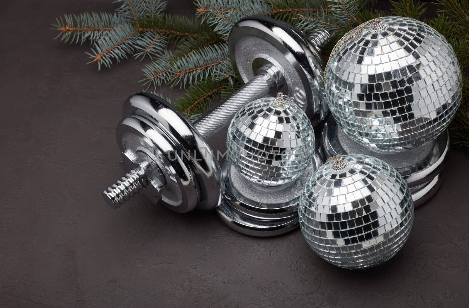Sports equipment (dumbbell with weights), fir branch, Christmas ornament on dark grey background. Top view. Fitness, sport or healthy lifestyle concept. New Year and Christmas.