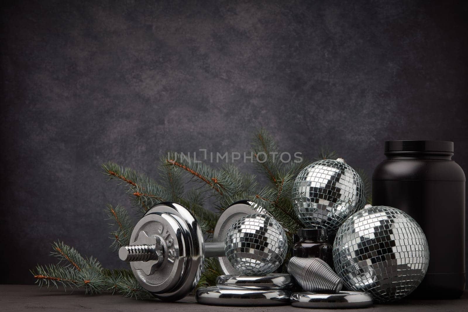 Sports nutrition (supplements), sports equipment, branch of fir, Christmas ornaments on dark grey background with copy space. Fitness, sport or healthy lifestyle concept. New Year and Christmas.