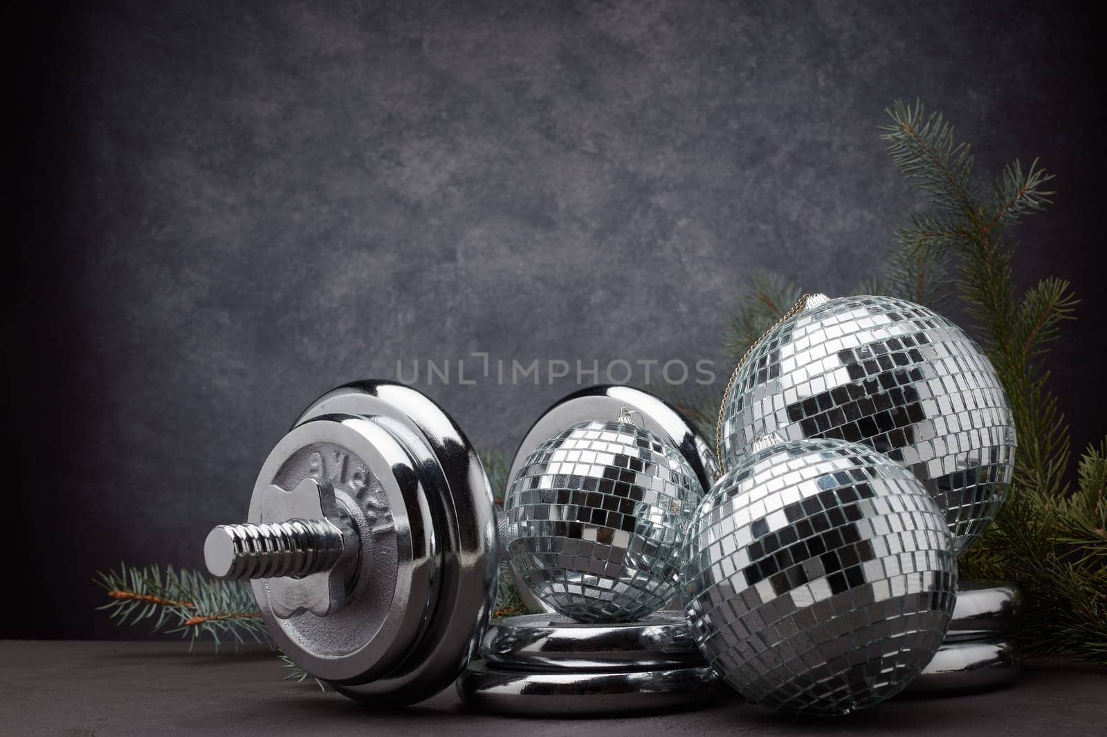 Sports equipment (dumbbell with weights), fir branch, Christmas ornament on dark grey background with copy space. Fitness, sport or healthy lifestyle concept. New Year and Christmas.