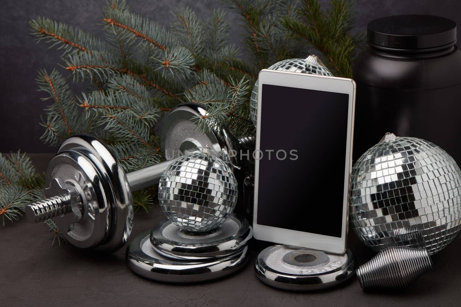 Sports nutrition, sports equipment, fir branch, Christmas ornament, blank computer tablet on dark grey background. Fitness, sport or healthy lifestyle concept. New Year and Christmas.