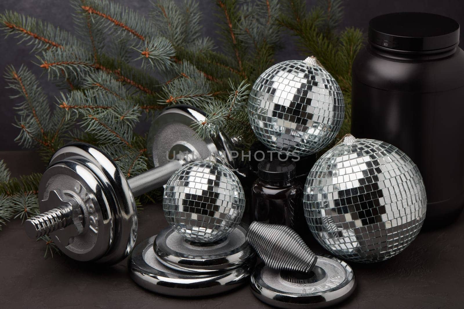 Sports nutrition (supplements), sports equipment, branch of fir, Christmas ornaments on dark grey background. Fitness, sport or healthy lifestyle concept. New Year and Christmas.