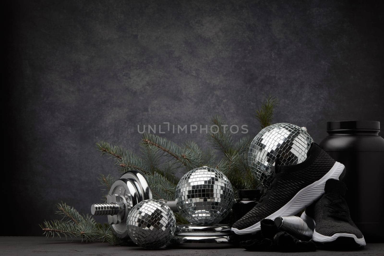 Sports nutrition (supplements), sports equipment, branch of fir, Christmas ornaments on dark grey background with copy space. Fitness, sport or healthy lifestyle concept. New Year and Christmas.