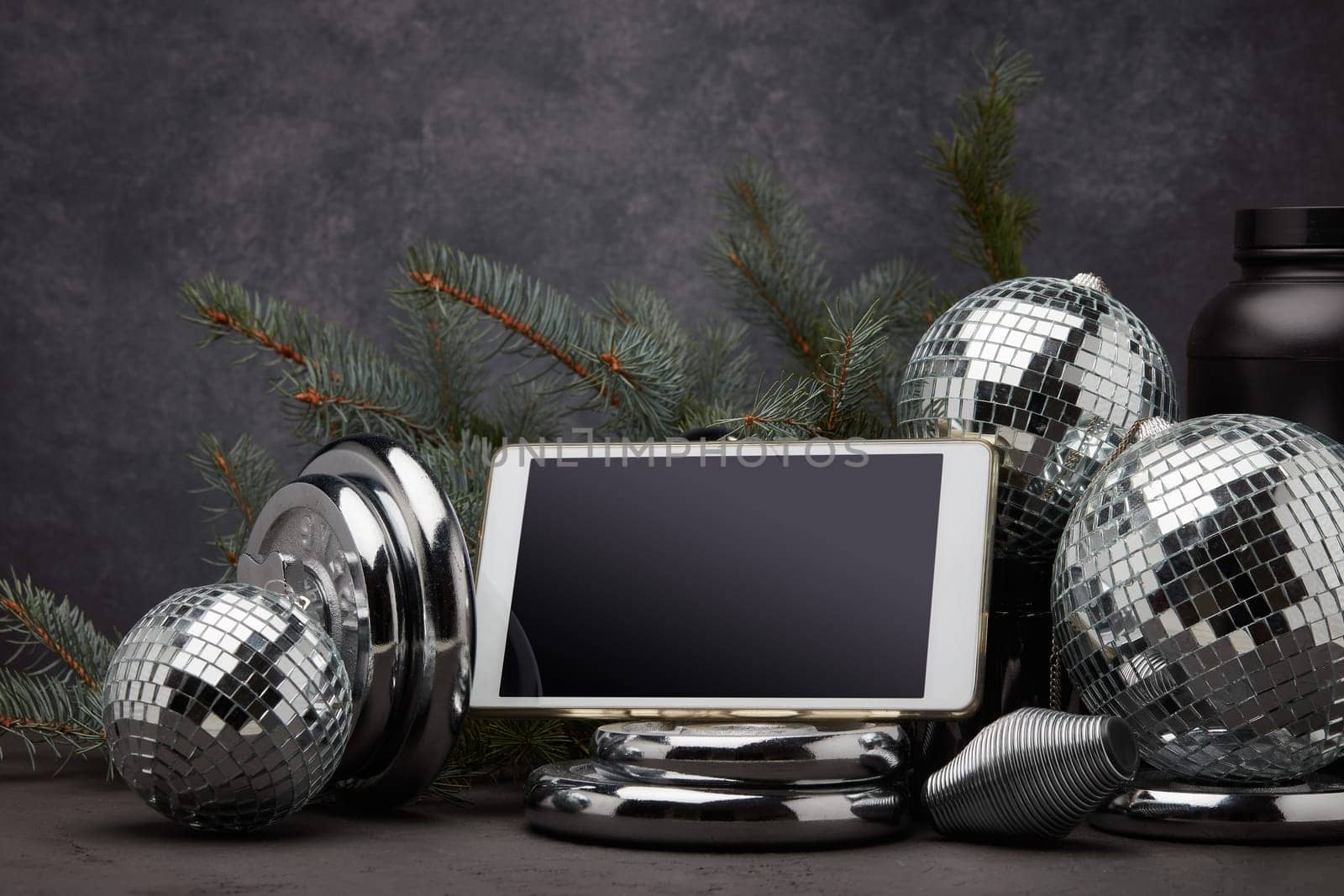 Sports nutrition, sports equipment, fir branch, Christmas ornament, blank computer tablet on dark grey background. Fitness, sport or healthy lifestyle concept. New Year and Christmas.