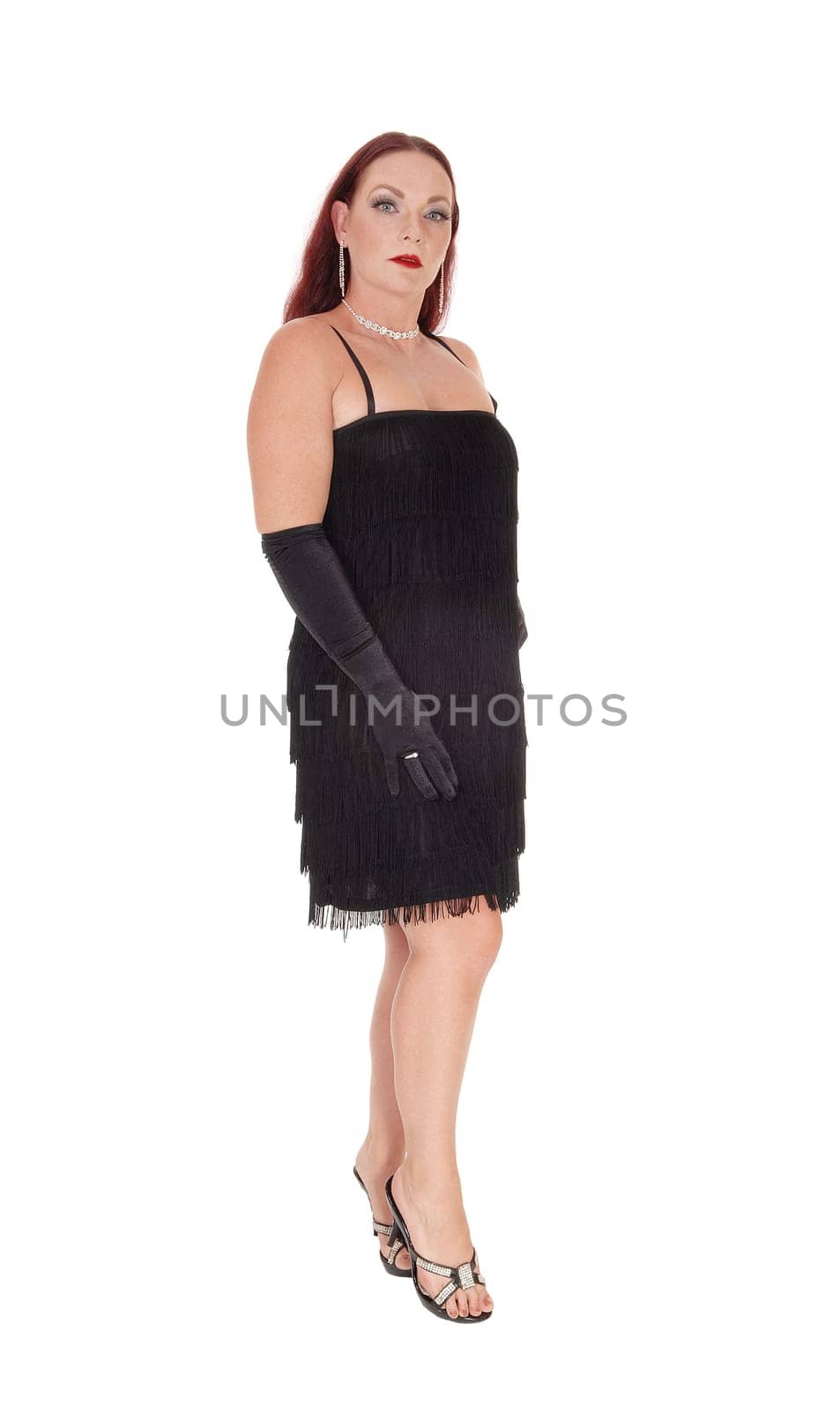 A beautiful woman standing in a black dress in profile with her long.red hair falling in the back and cloves, isolated for white background.