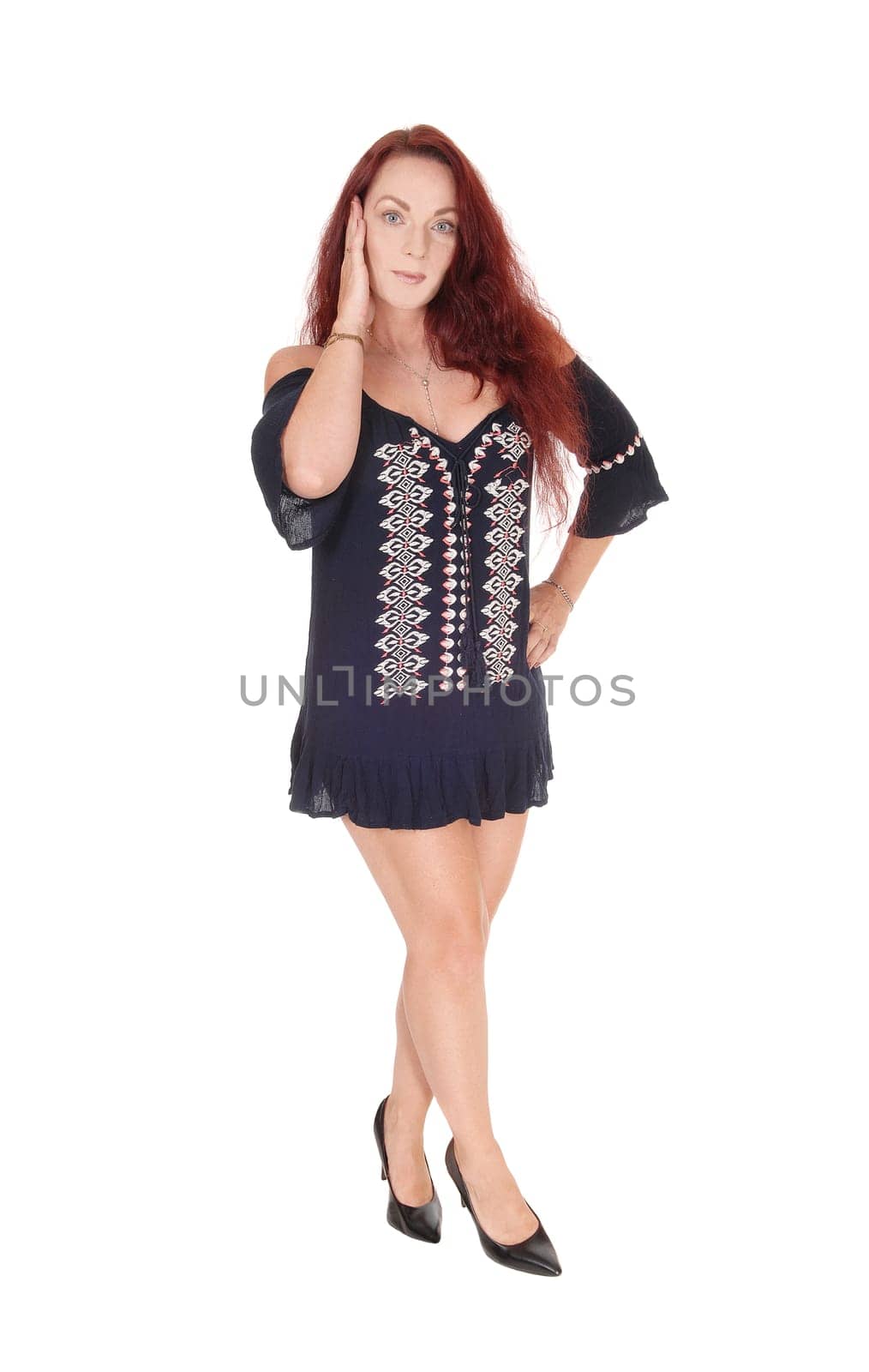 A middle age beautiful woman standing from the front in a short.black dress with one hand on her face, isolated for white background.