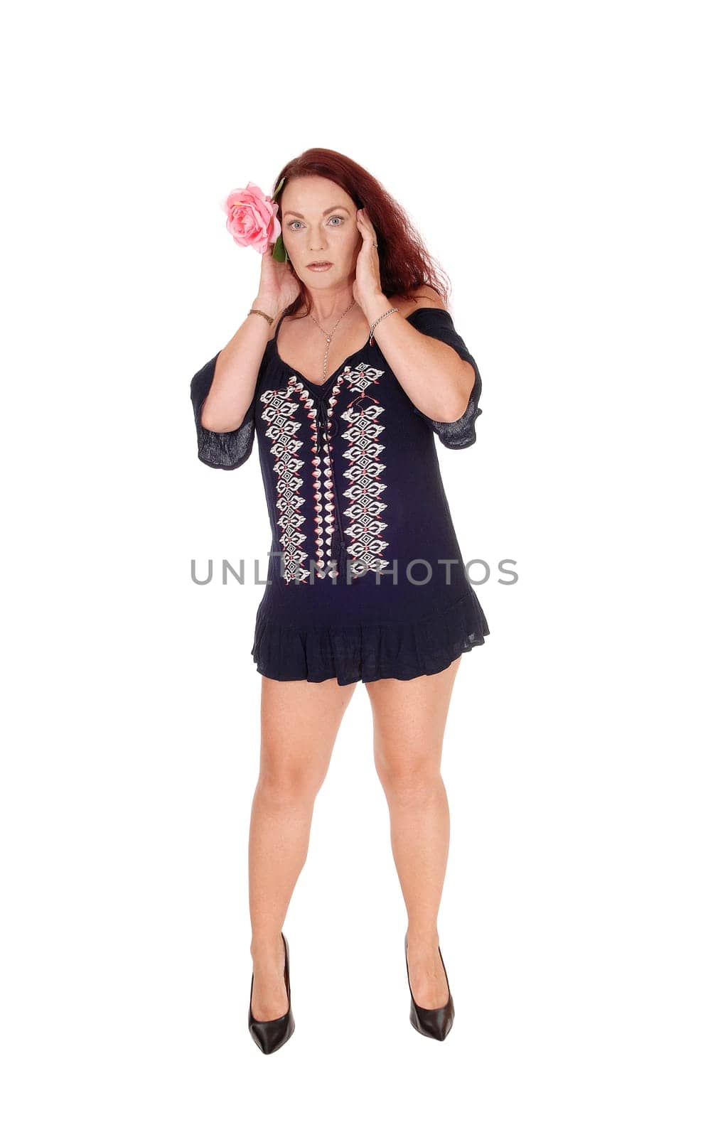 A middle age beautiful woman standing in the profile in a short.black dress with her hands on her face, isolated for white background.