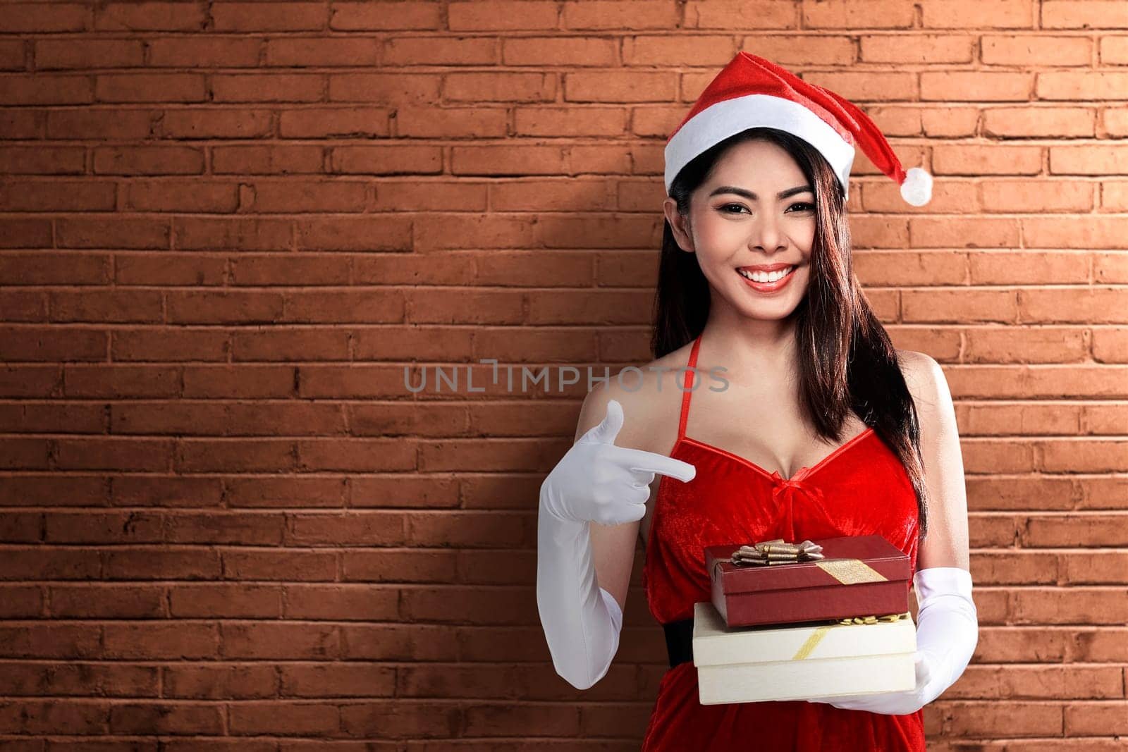 Asian woman in Santa costume holding gift box with brick wall background