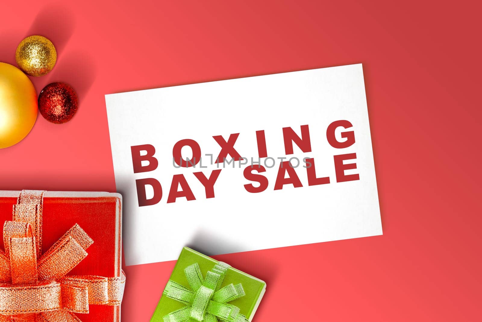 Gift box with a ribbon and Christmas ornament with Boxing Day Sale text on paper over the red background