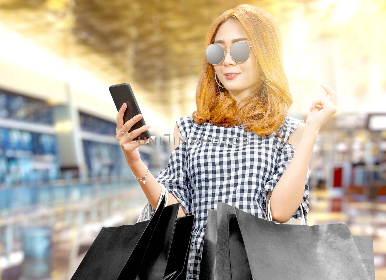 Asian woman using the mobile phone while holding black shopping bags in the mall. Black Friday concept