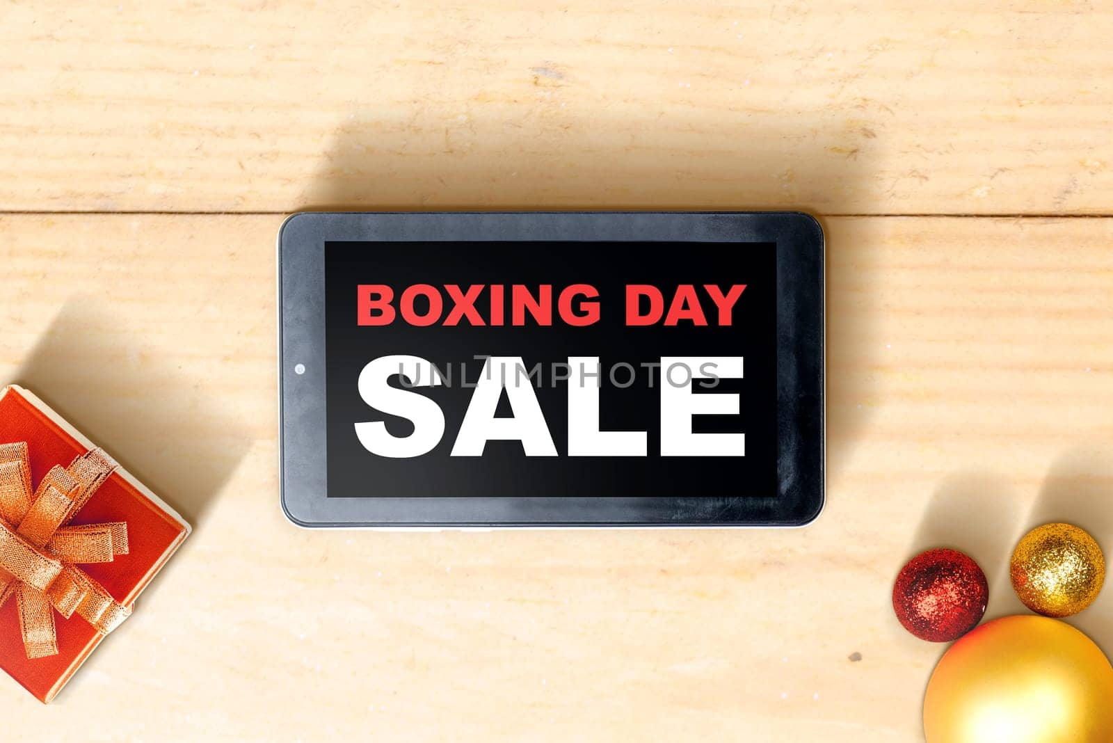 Gift box with a ribbon and Christmas ornament with Boxing Day Sale text on tablet screen with wooden table background