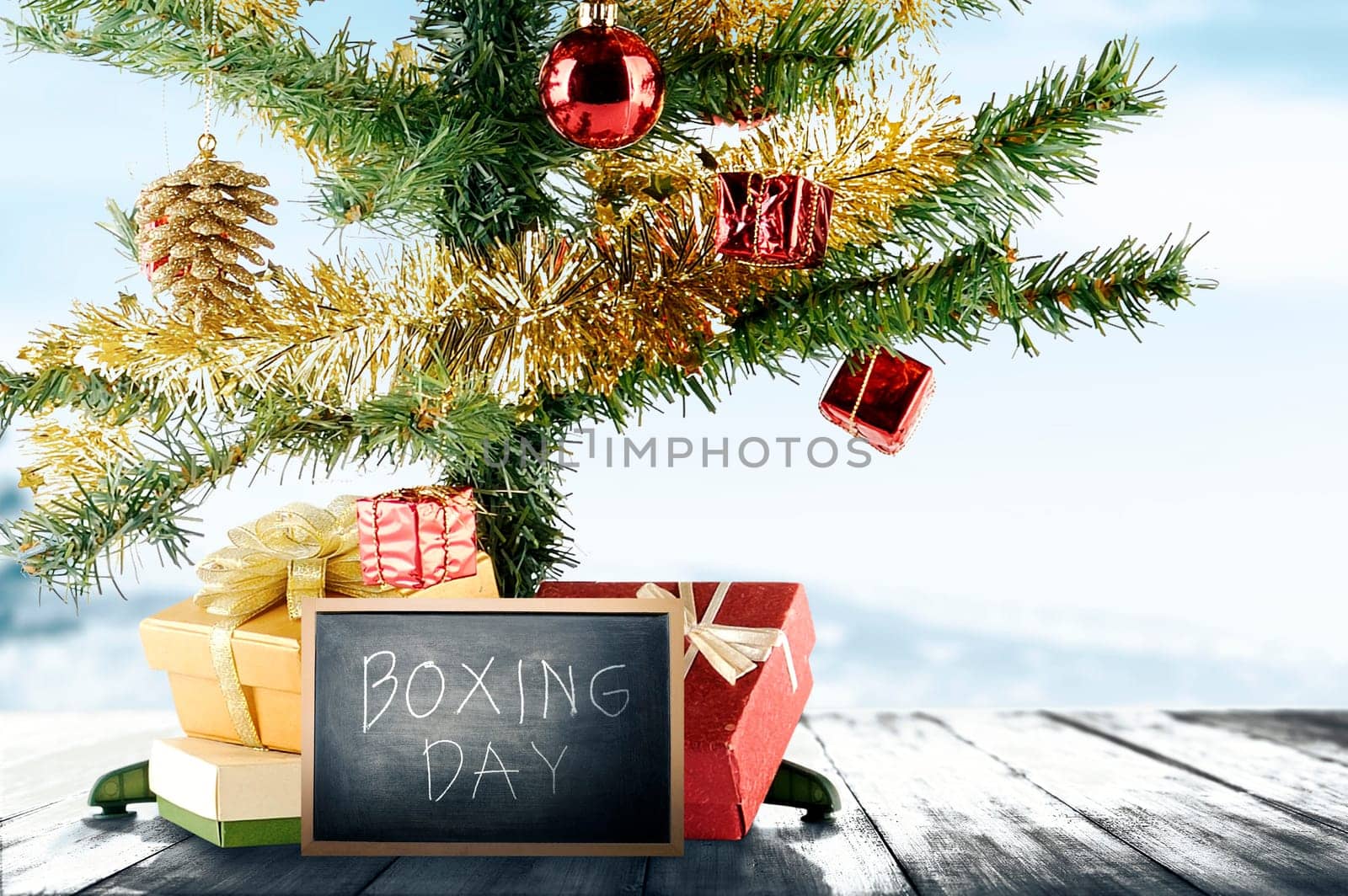 Christmas tree with gift box and Boxing Day text on the blackboard on wooden floor with a snowy background