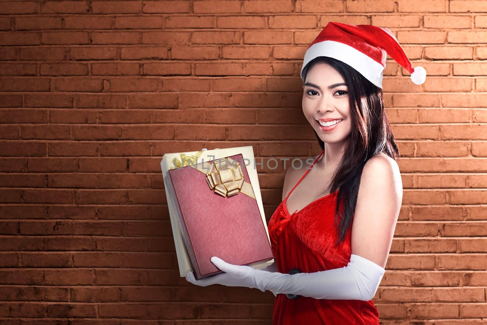 Asian woman in Santa costume holding gift box with brick wall background