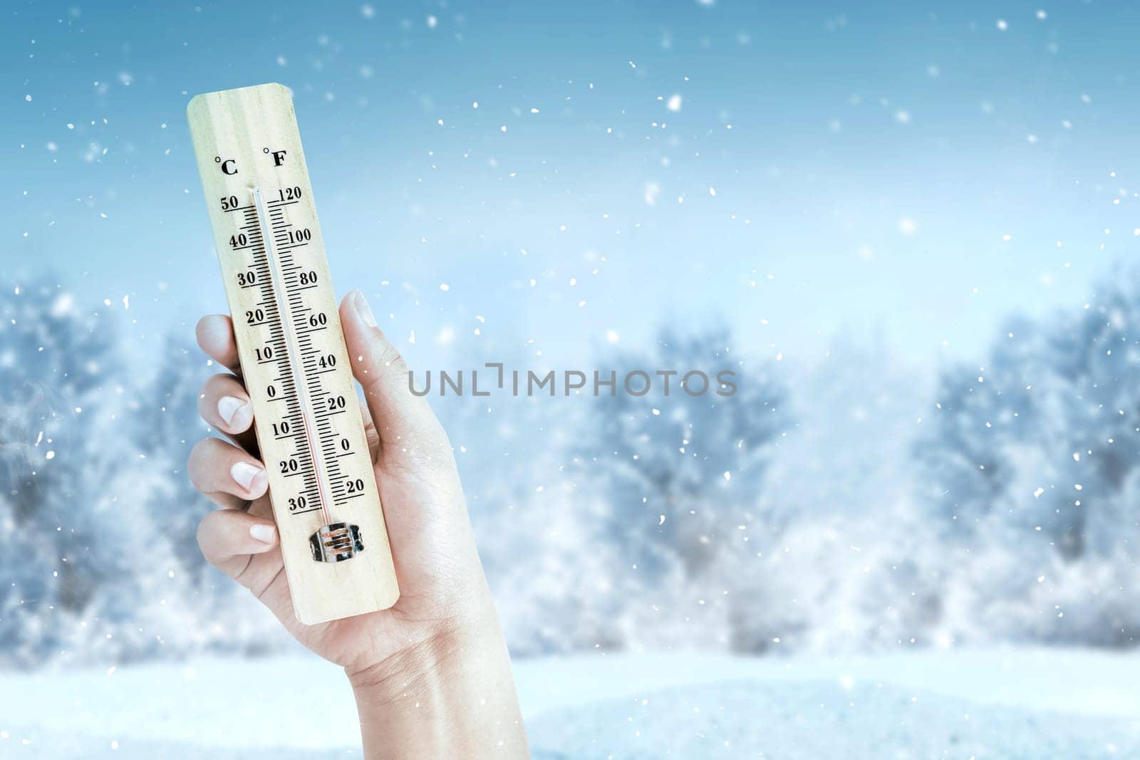 Hand holding wooden thermometer with the low temperature at winter with snowfall background