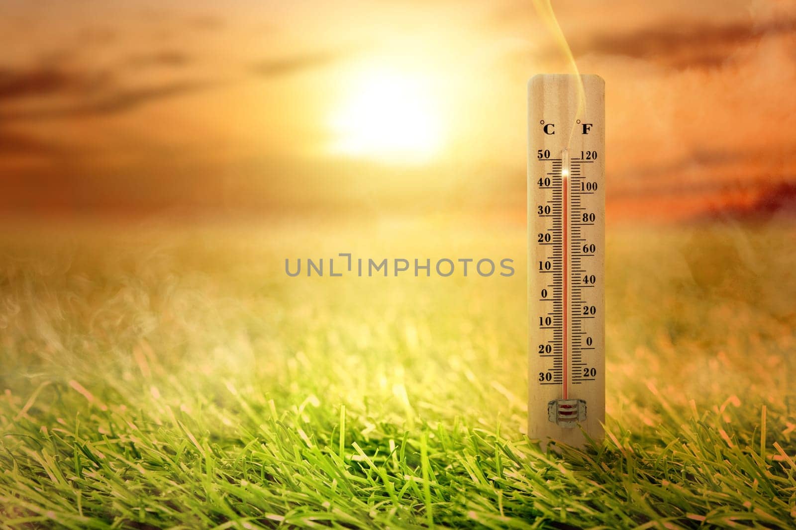 Thermometer with high temperature on the meadow with glowing sun background. Heatwave concept