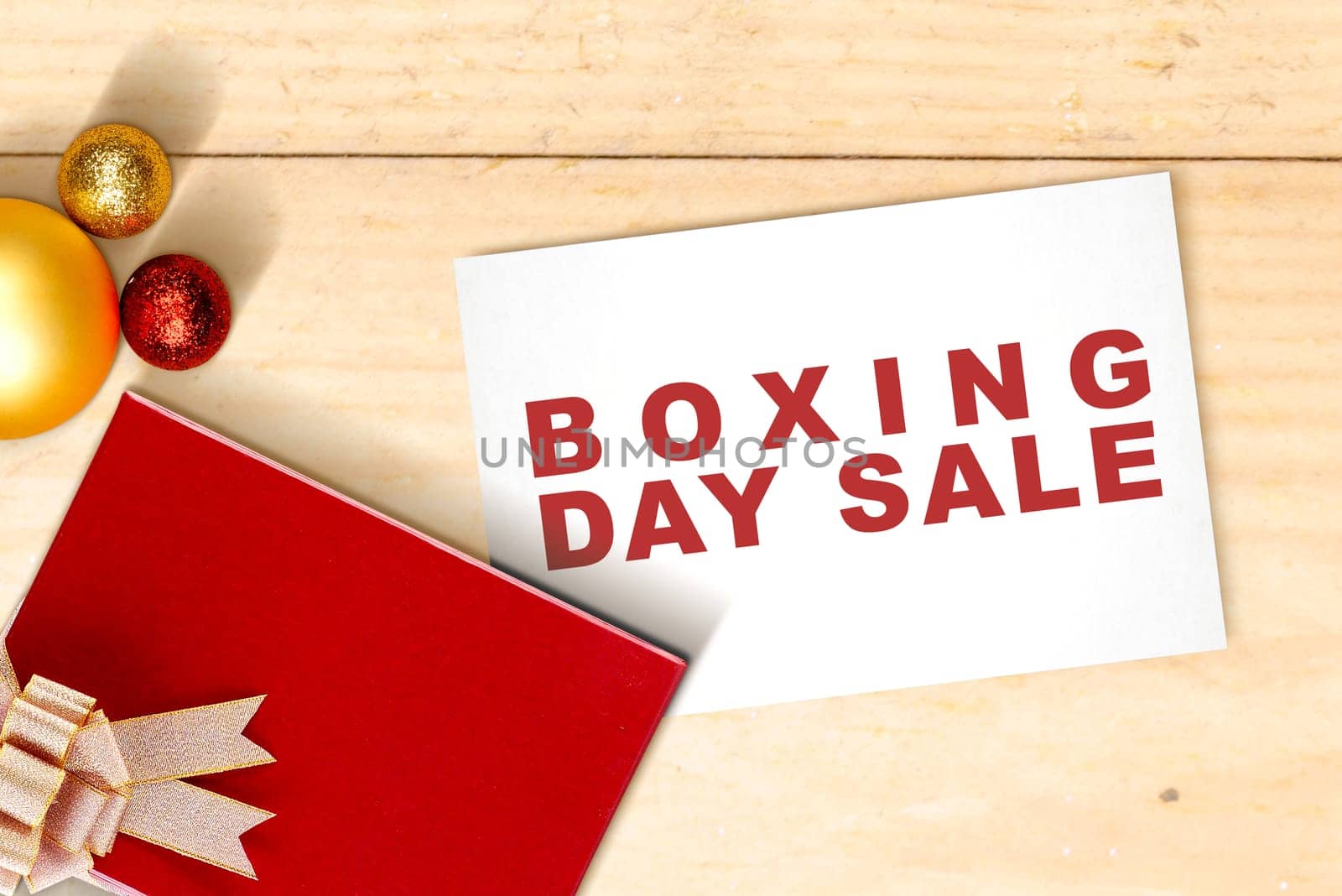 Gift box with a ribbon and Christmas ornament with Boxing Day Sale text on paper with wooden table background
