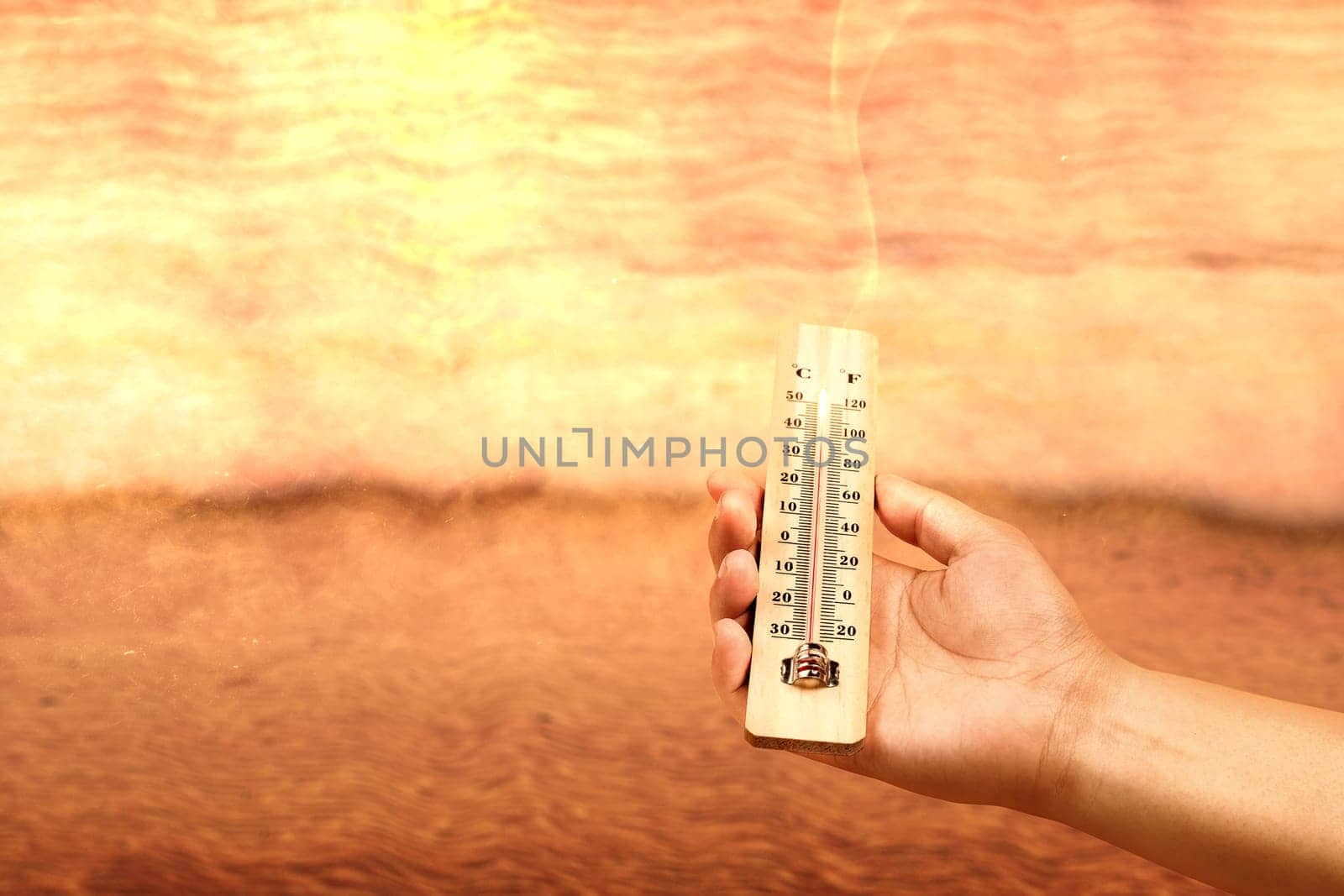 Hand holding thermometer with high temperature on the beach with glowing sun background. Heatwave concept
