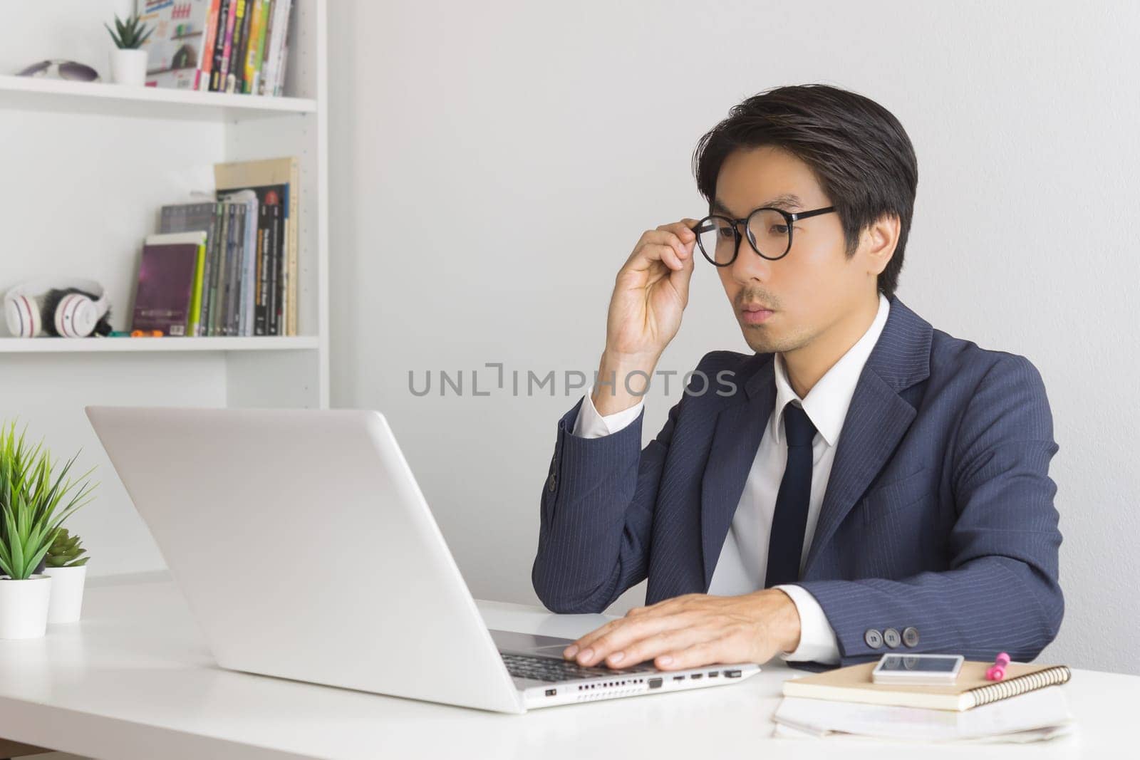 Asian Financial Advisor or Asian Consulting Businessman in Suit Consider and Analyze Financial Data. Asian Financial Advisor or Asian Consulting Businessman serious working in office