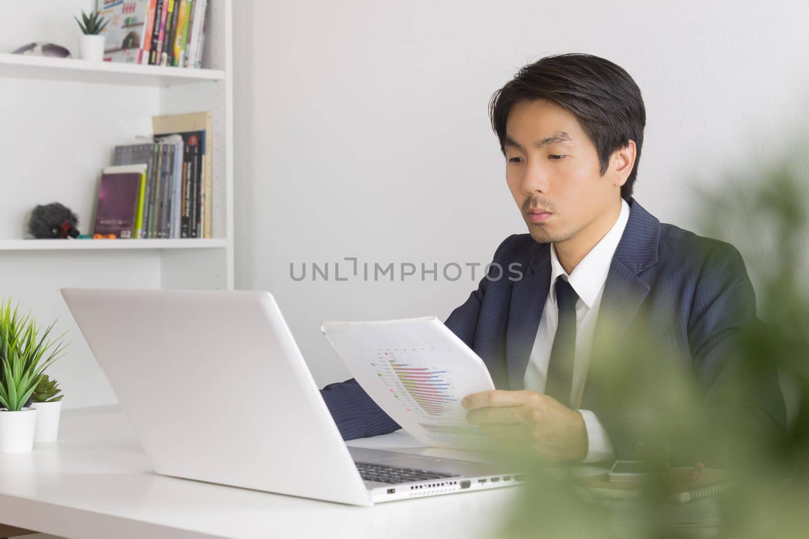 Asian Financial Advisor or Asian Consulting Businessman Analyze Financial Report in front of Laptop. Asian financial advisor or Asian consulting businessman working in office