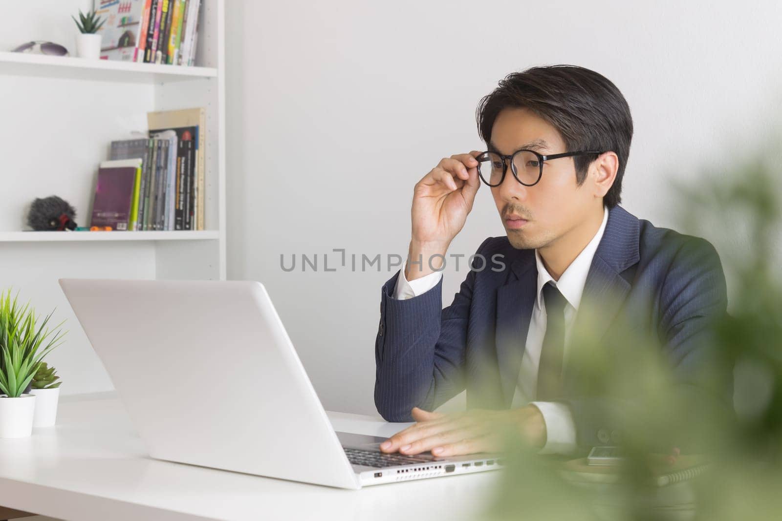 Asian Financial Advisor or Asian Consulting Businessman Seriously Calculate the Financial Data in front of Laptop. Asian financial advisor or Asian consulting businessman working in office